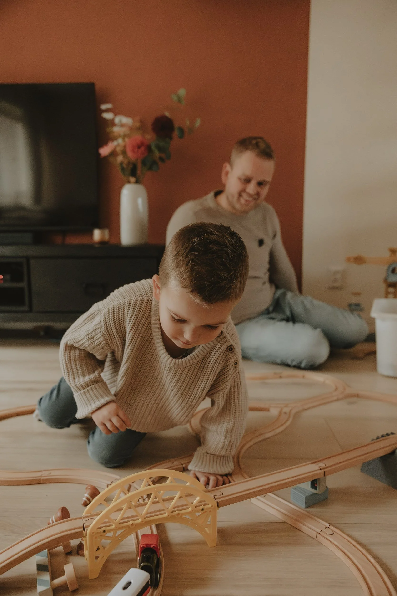 Gezinsfotografie aan huis in Emmen – jongen speelt met houten treinbaan terwijl vader toekijkt tijdens lifestyle familieshoot