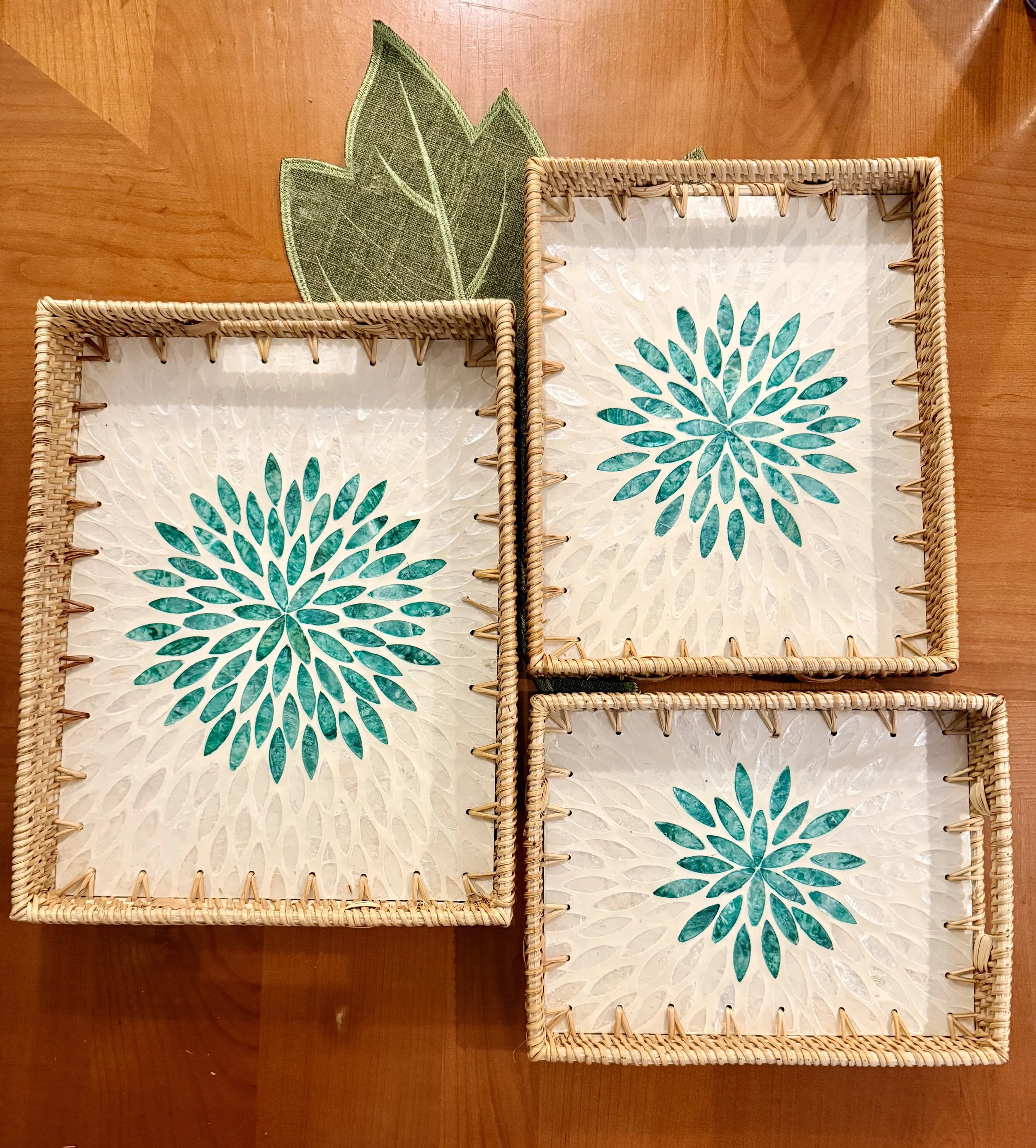 Three rectangular woven baskets with white and teal floral design liners, placed on a wooden surface, with a green leaf placemat nearby.
