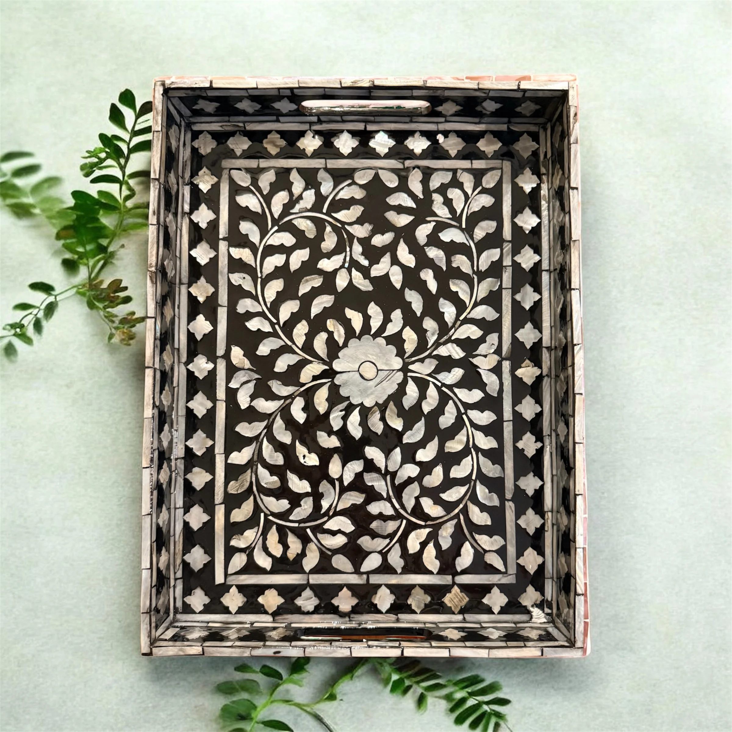 Decorative metal tray with floral and leaf patterns, placed on a light green surface with green foliage nearby.