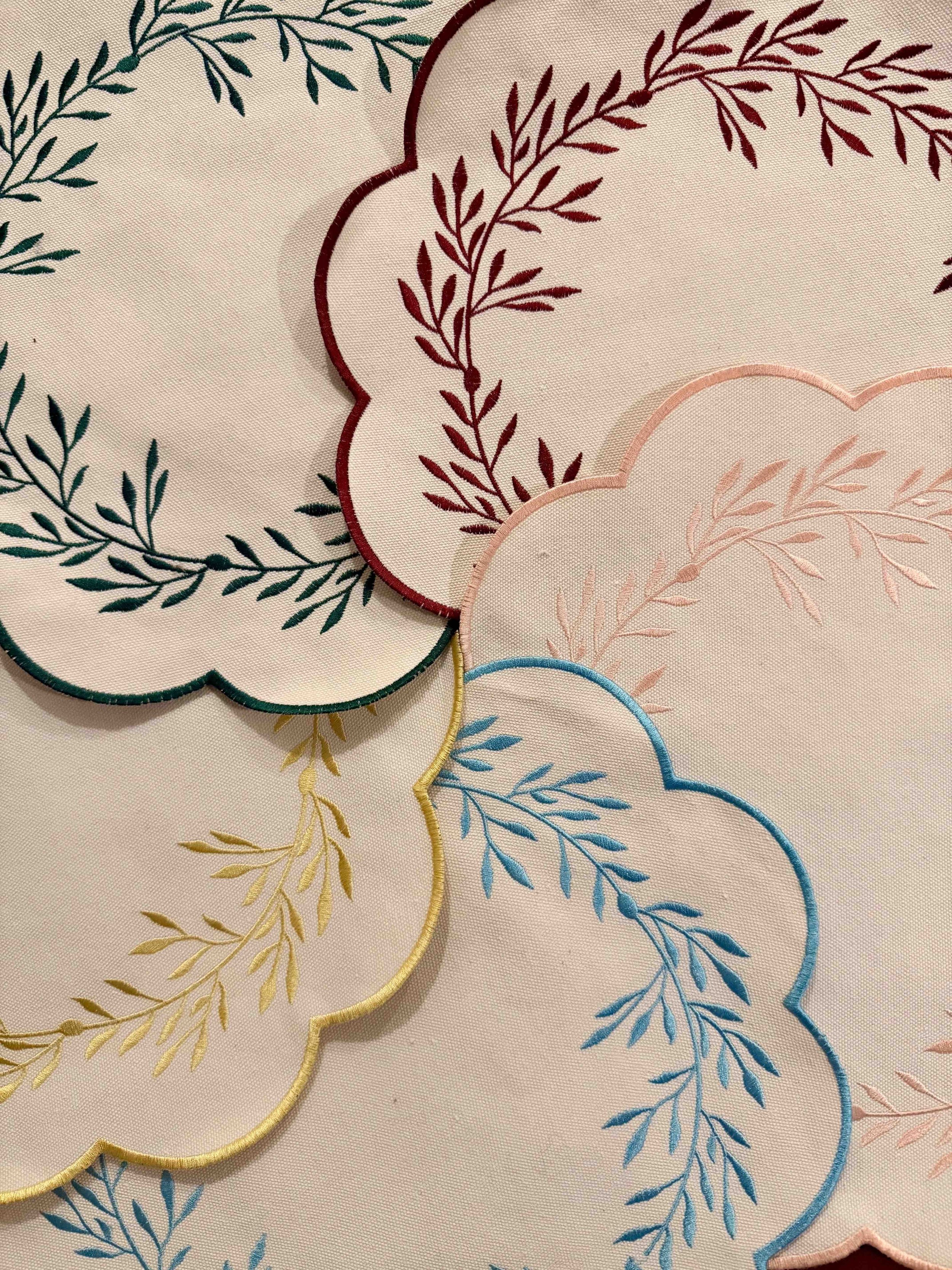 Close-up of embroidered fabric with overlapping floral patterns in different colors, including green, red, pink, blue, and yellow, with scalloped edges.