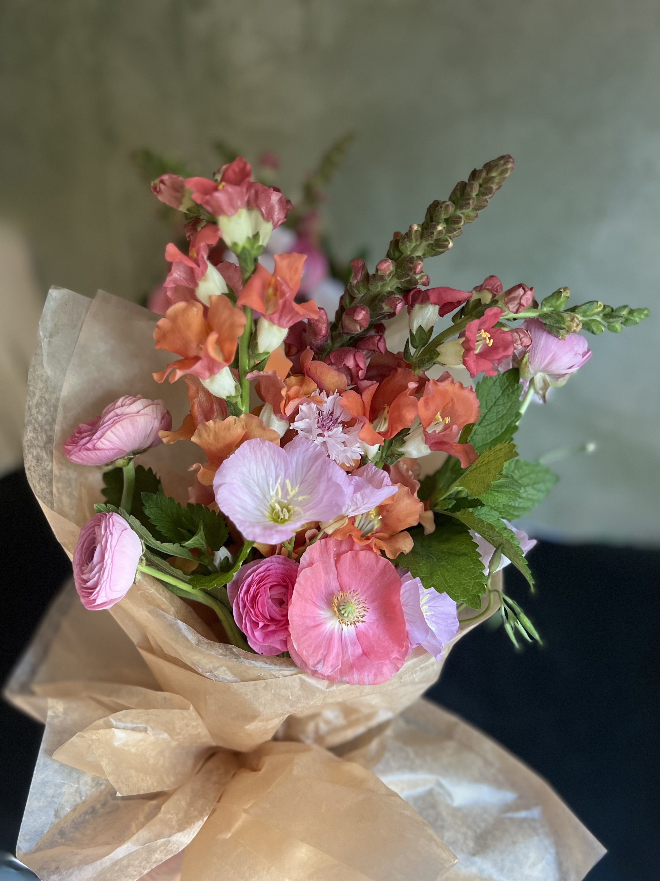 A bouquet of pink, orange, and purple flowers wrapped in brown paper.