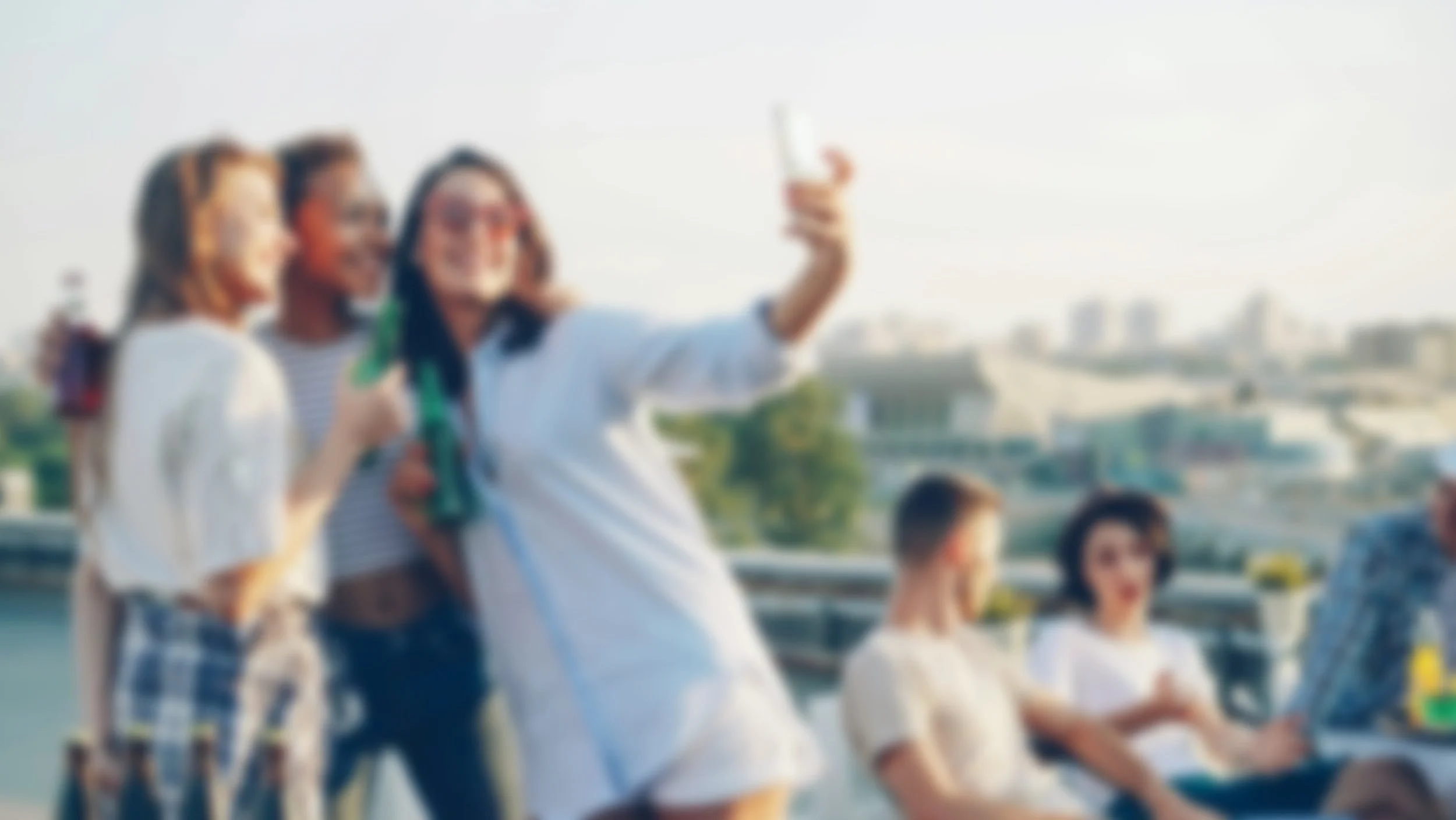 A group of friends taking a selfie together outdoors during daytime, with a cityscape in the background.
