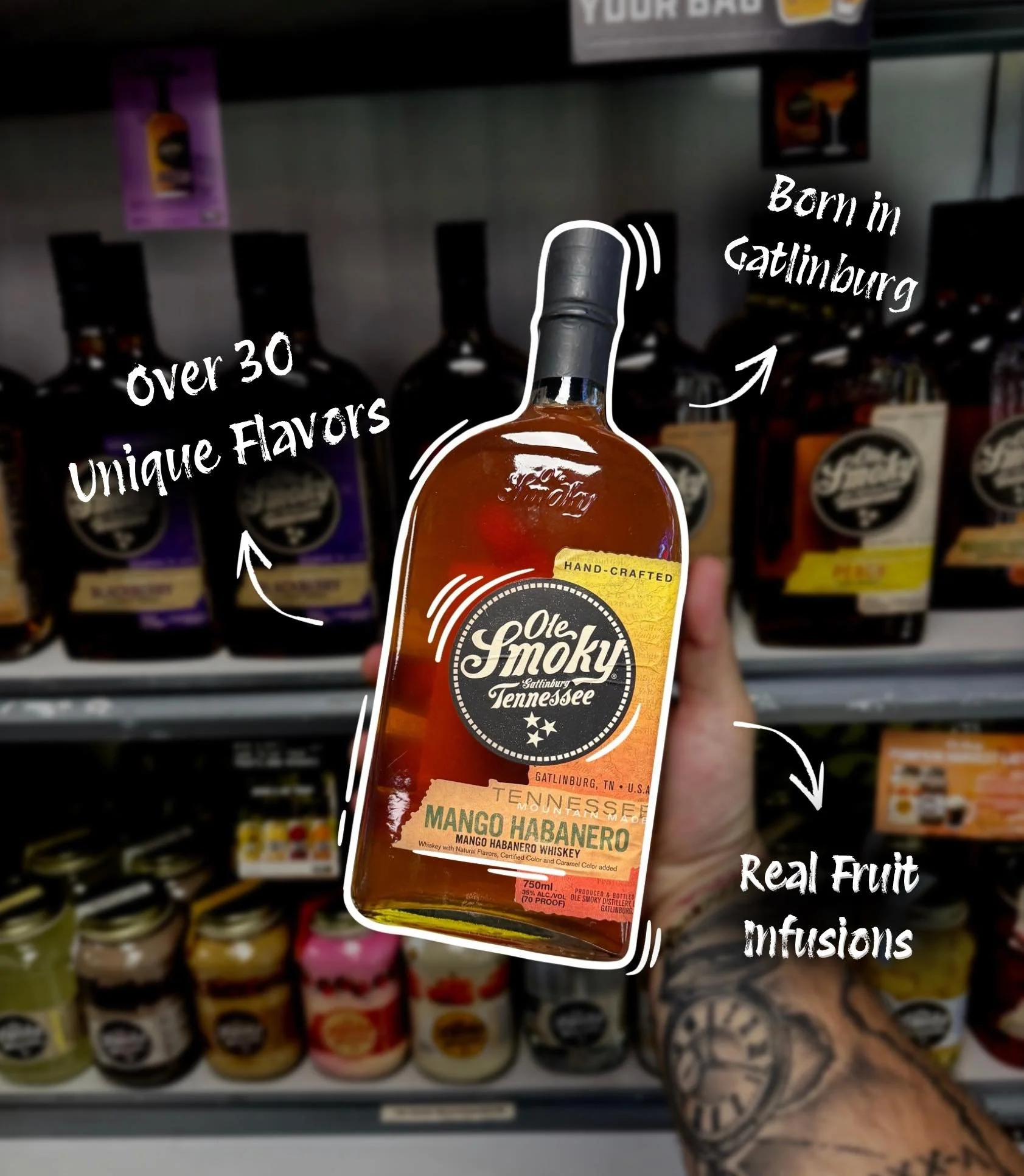 A hand holding a bottle of Ole Smoky Mango Habanero whiskey in a store, with annotations indicating it is made in Gatlinburg, Tennessee, contains real fruit infusions, has over 30 unique flavors, and is hand-crafted.