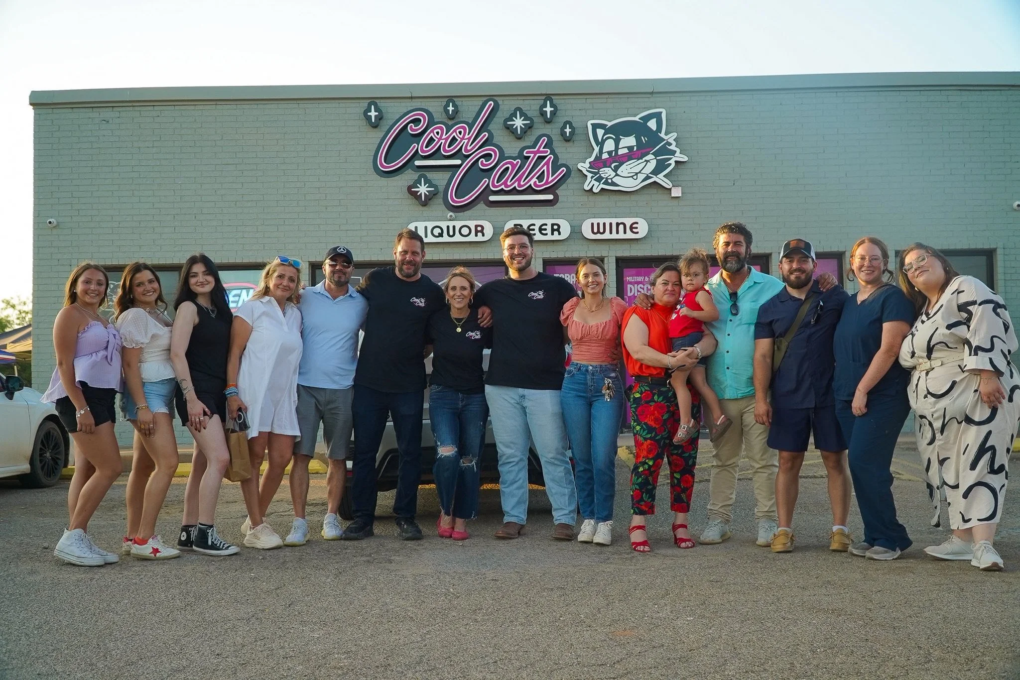 Group of people standing in front of a building with a sign that reads 'Cool Cats' and icons for liquor, beer, and wine.
