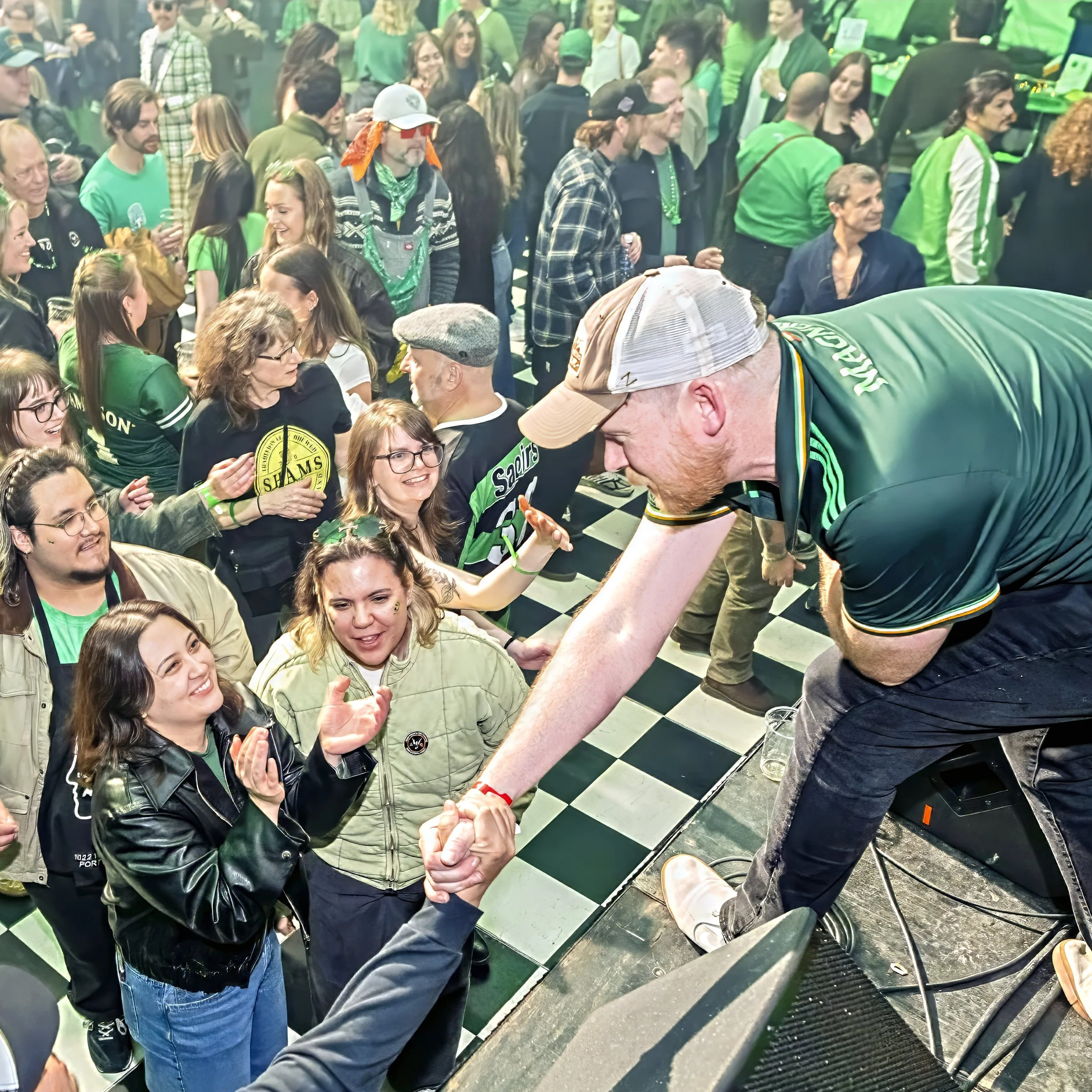 Matt Finn connecting with the crowd from the stage at a packed St. Patrick's Day show, fans in Shams merch cheering in the background.
