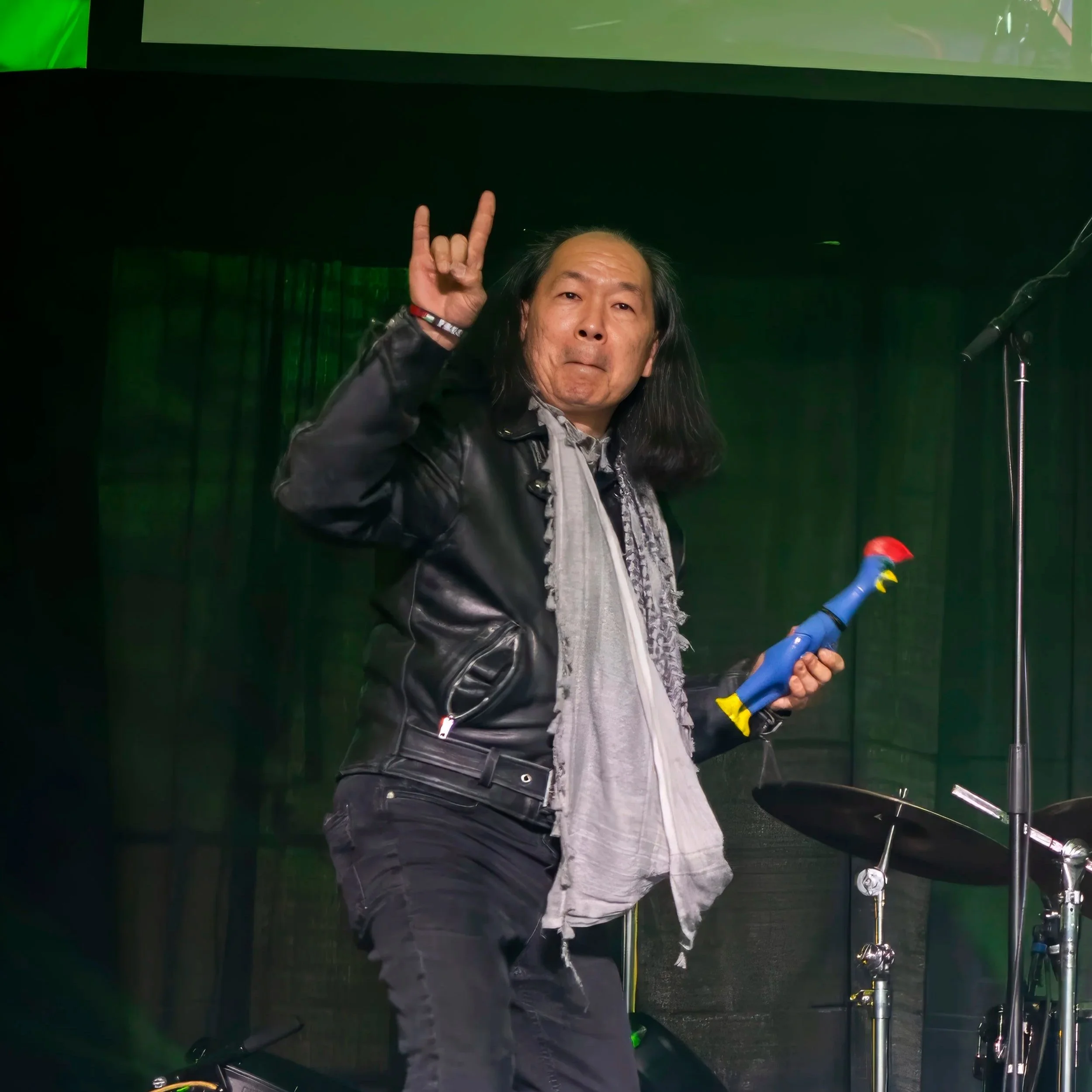 Franko of Sean Daly and The Shams on stage — rock horns up, rubber chicken in hand, bringing the chaos at a Portland St. Patrick's Day show.