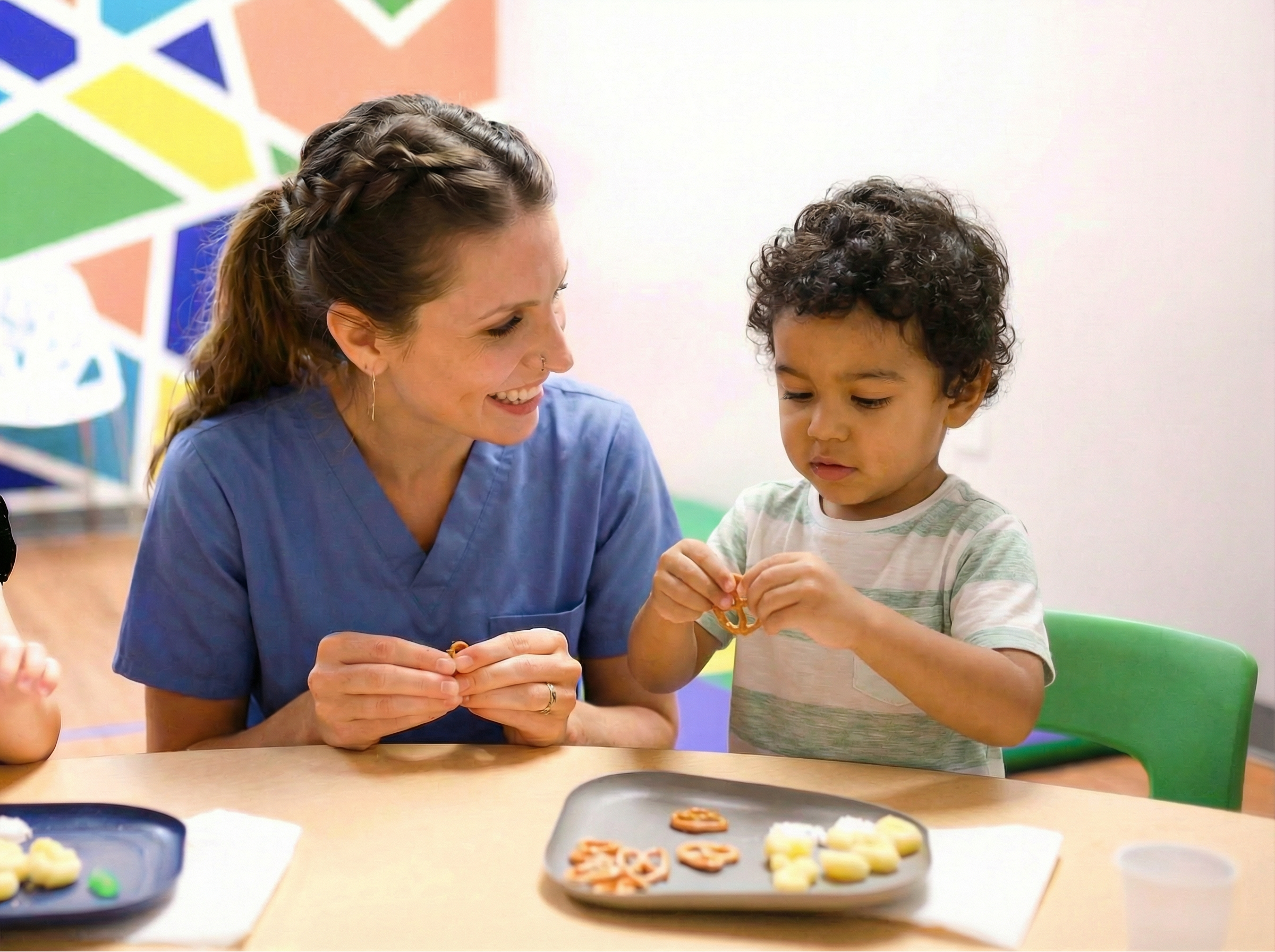 Child and speech therapist practice feeding skills at a table.