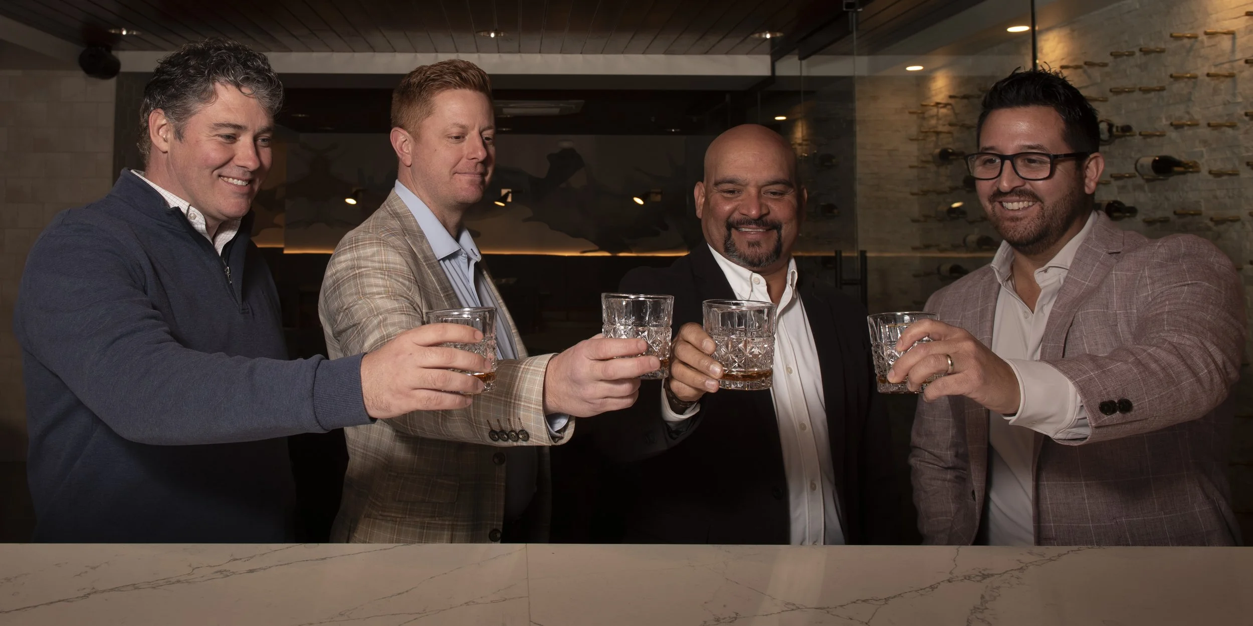 Four men in business attire enjoying drinks together in a bar or restaurant.