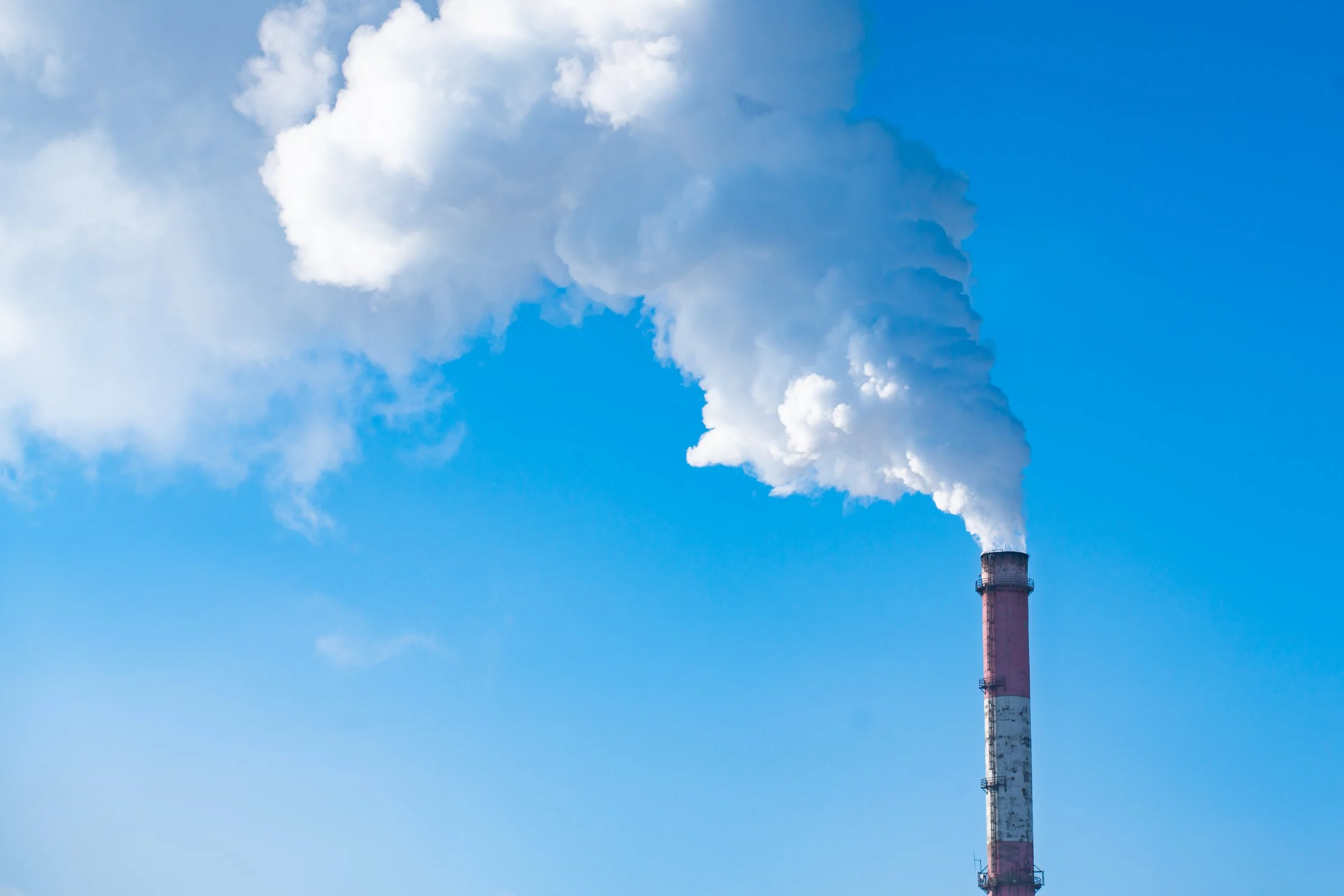 Industrial smokestack emitting white smoke into a clear blue sky.