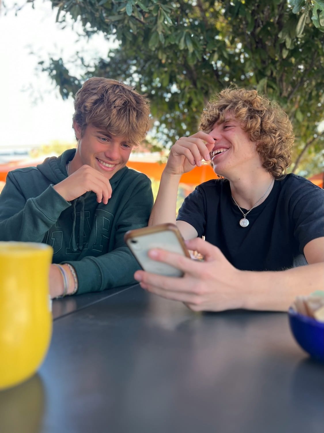 Two teenagers laughing joyfully together in sunny natural outdoor setting