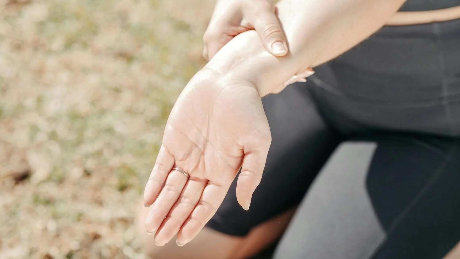 Person in athletic wear gently holding wrist showing joint awareness outdoors