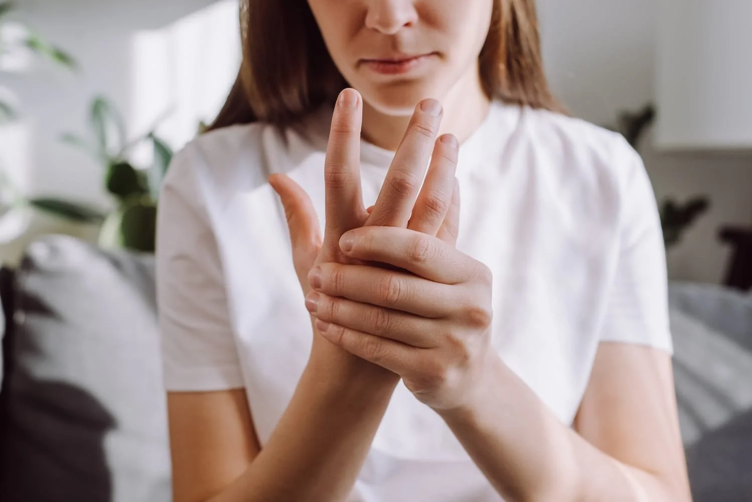 Young girl in white shirt gently holding hand showing finger joint discomfort
