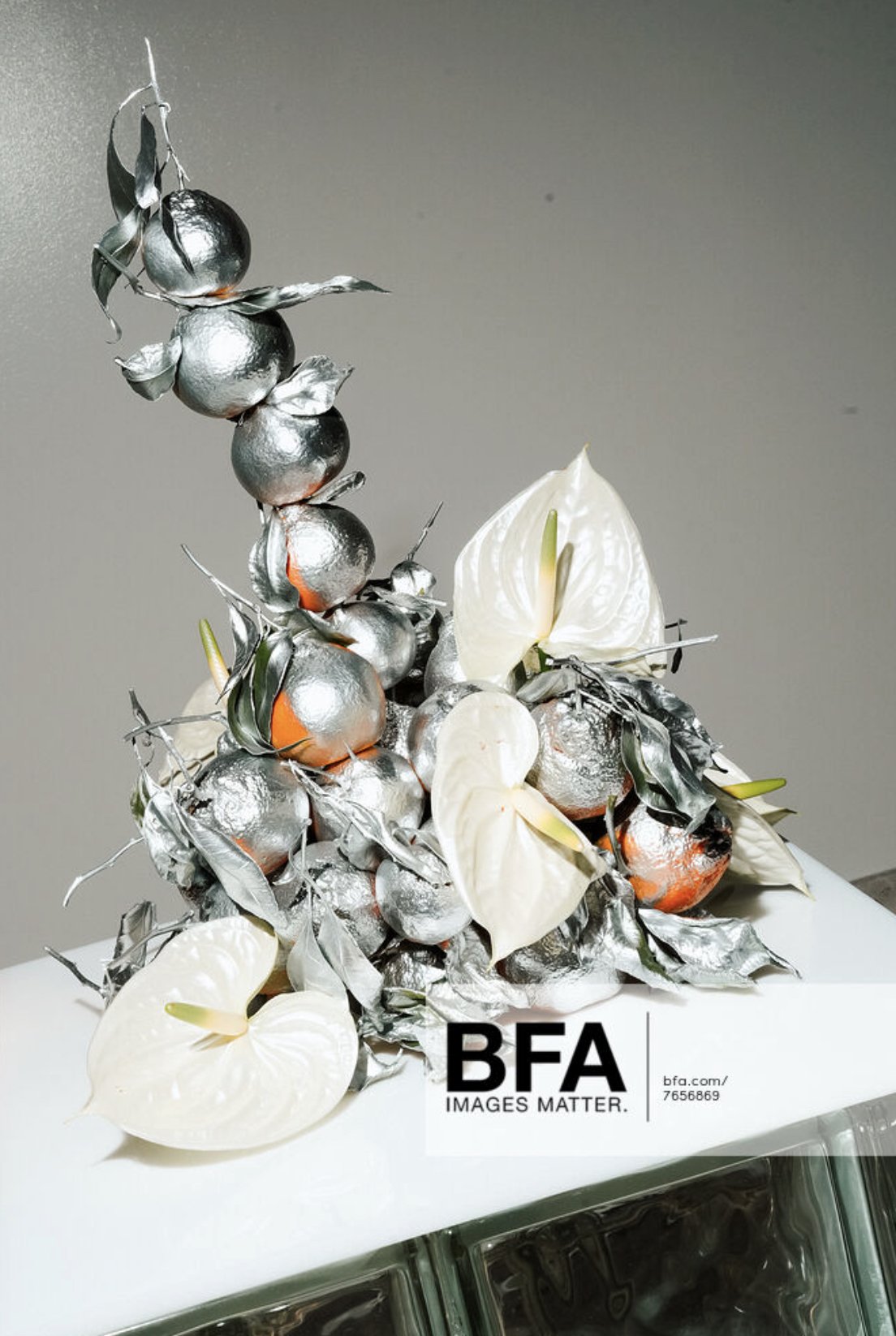 Artistic sculpture resembling a bunch of berries with silver metallic finish, accompanied by white anthurium flowers, placed on a white surface with a BFA Images Matter logo.