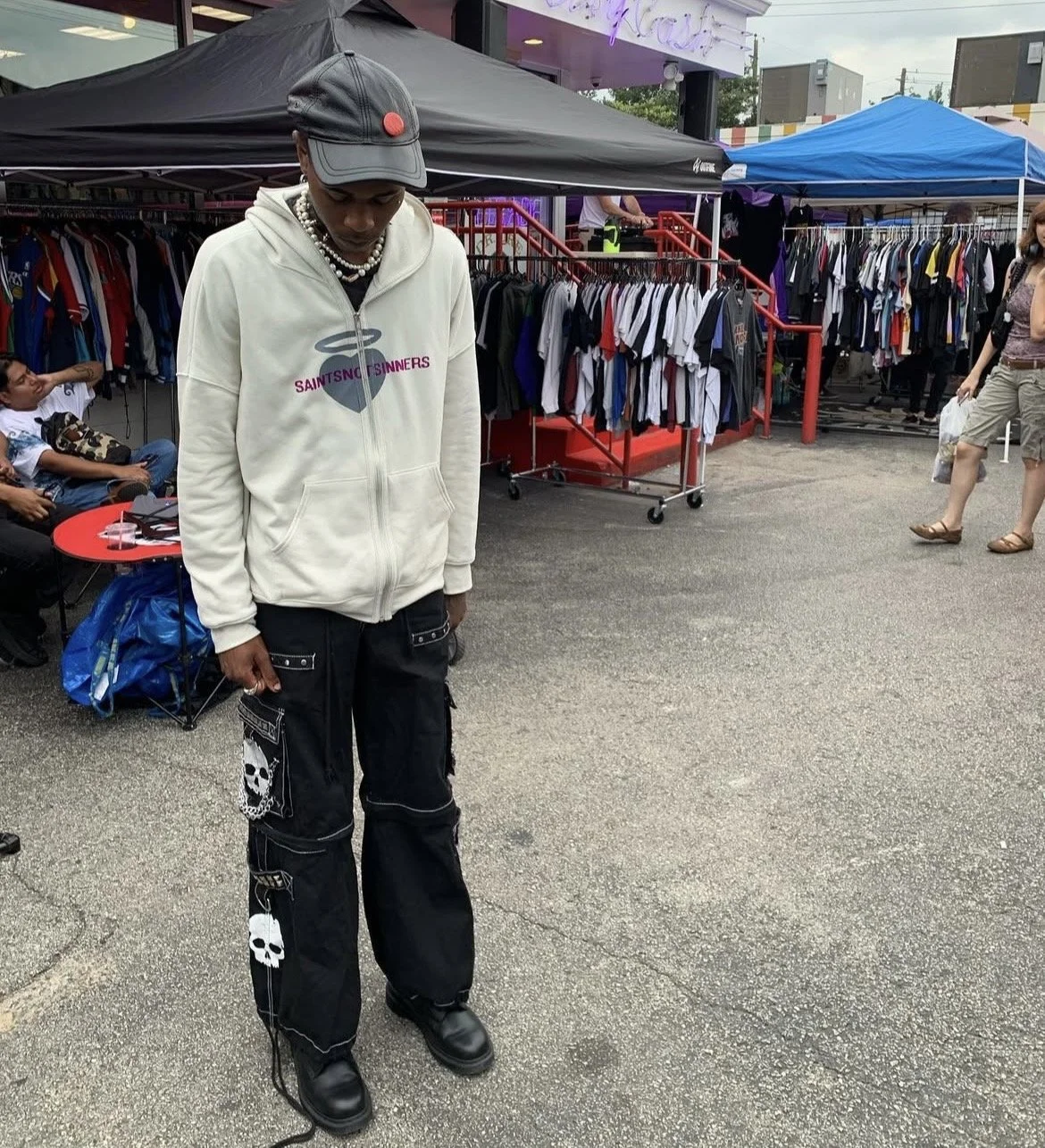 nilo standing at the thiftmarket on Westheimer in front of clothing racks with t-shirts, wearing a saintnotsinners zip up hoodie