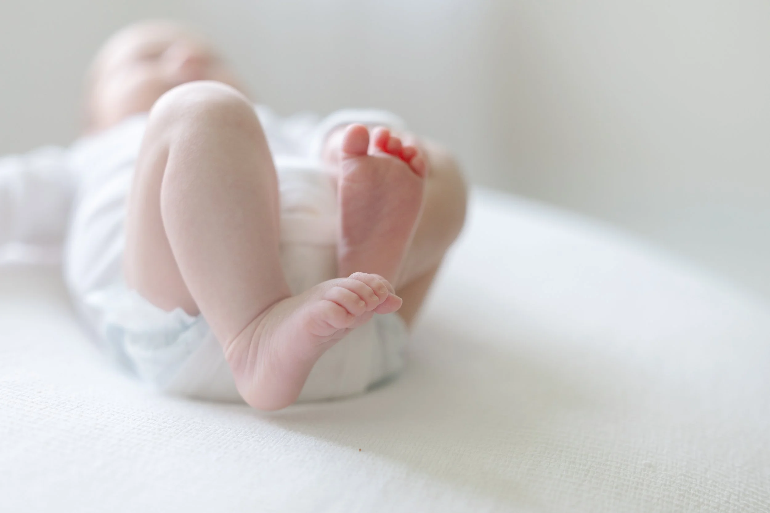 Close-up of a newborn baby's hand gripping an adult's finger, resting on a white surface.