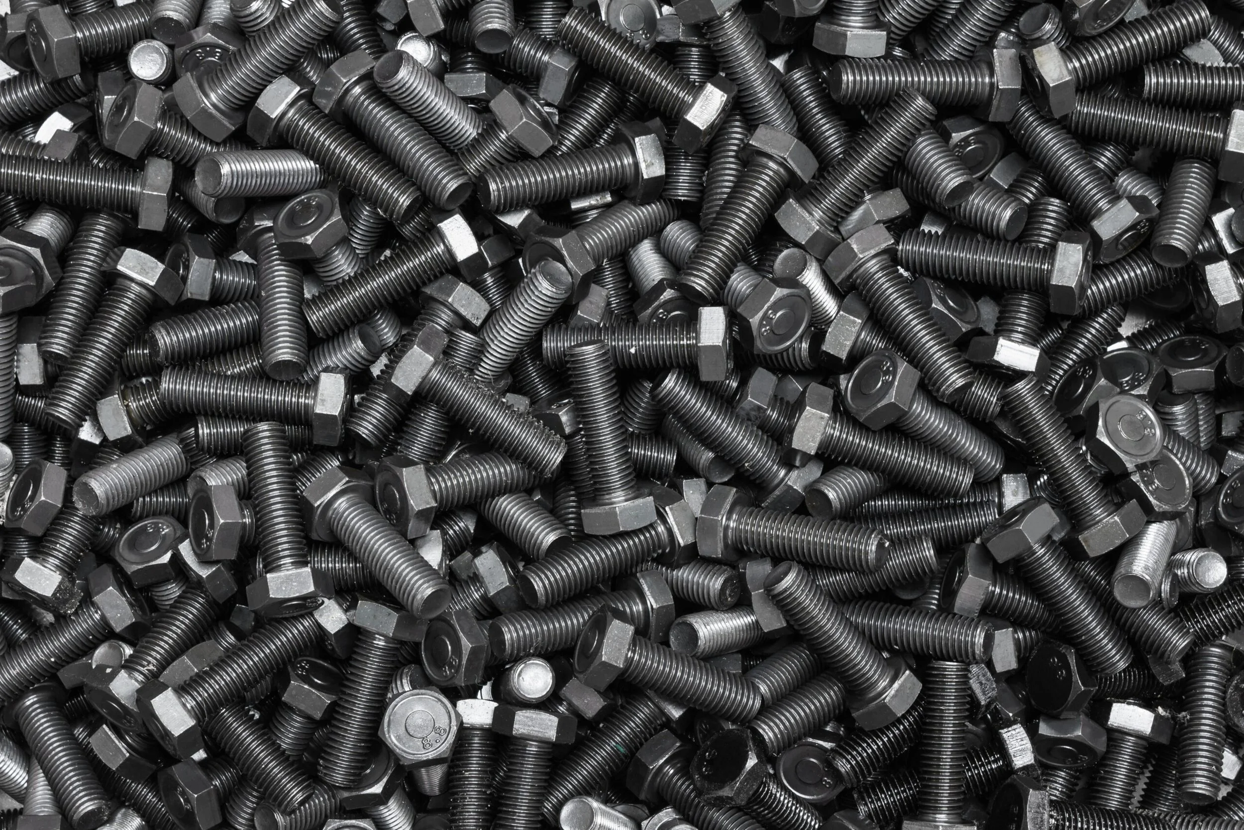 A large pile of black metal bolts with hexagonal heads.