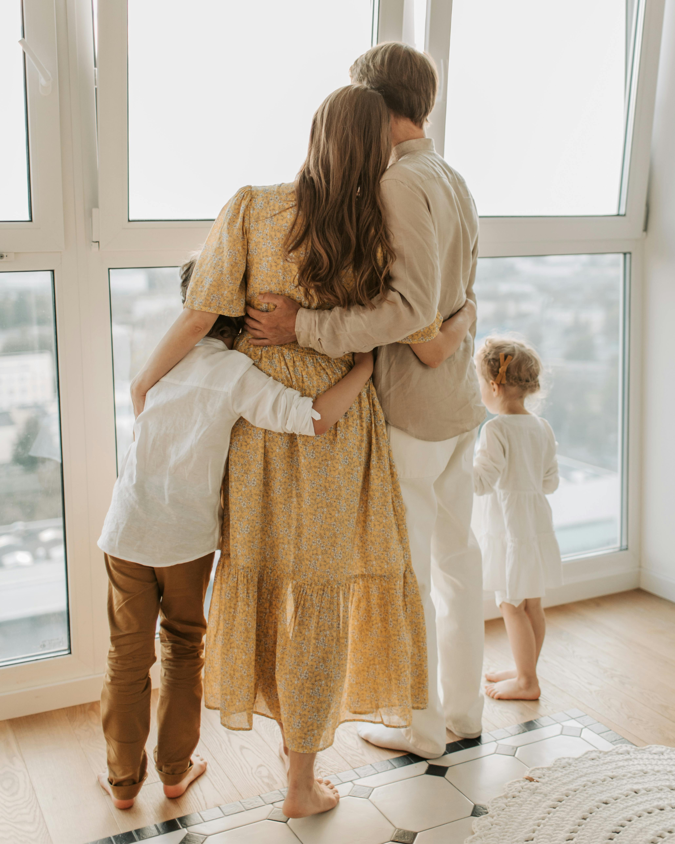 Family hugging near large windows, with children looking outside.