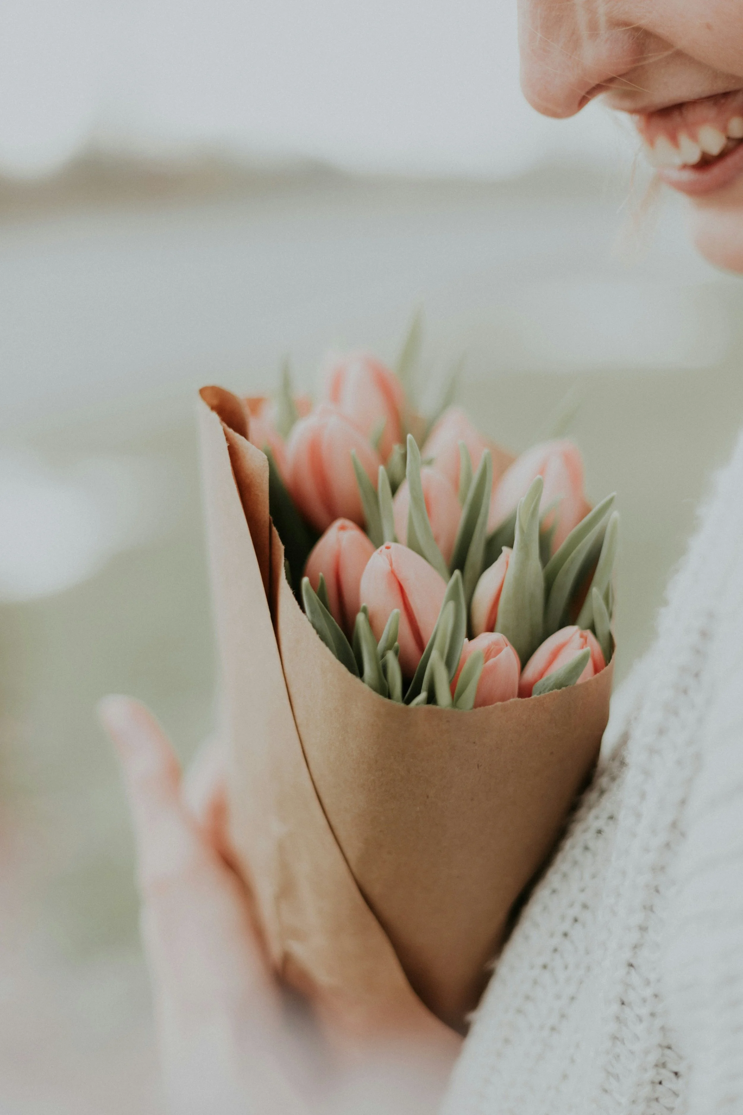 A person is holding a bouquet of pink tulips wrapped in brown paper.