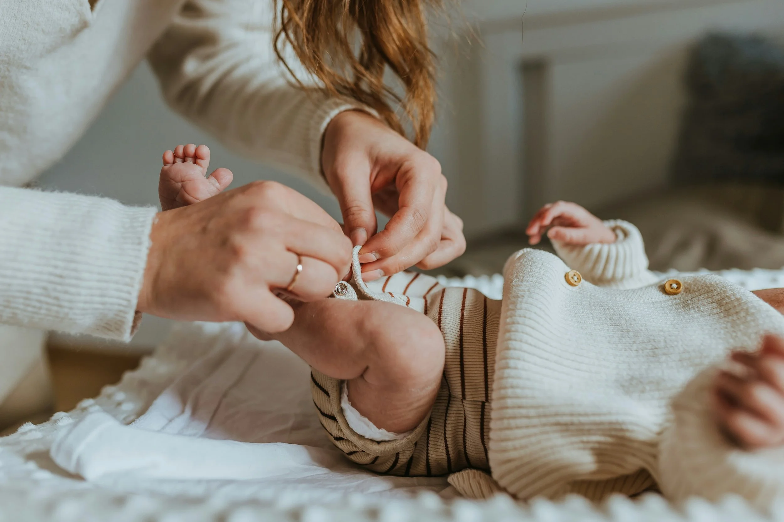 A person diapering a baby lying on a changing table, with the person's hands fastening the baby's striped outfit.