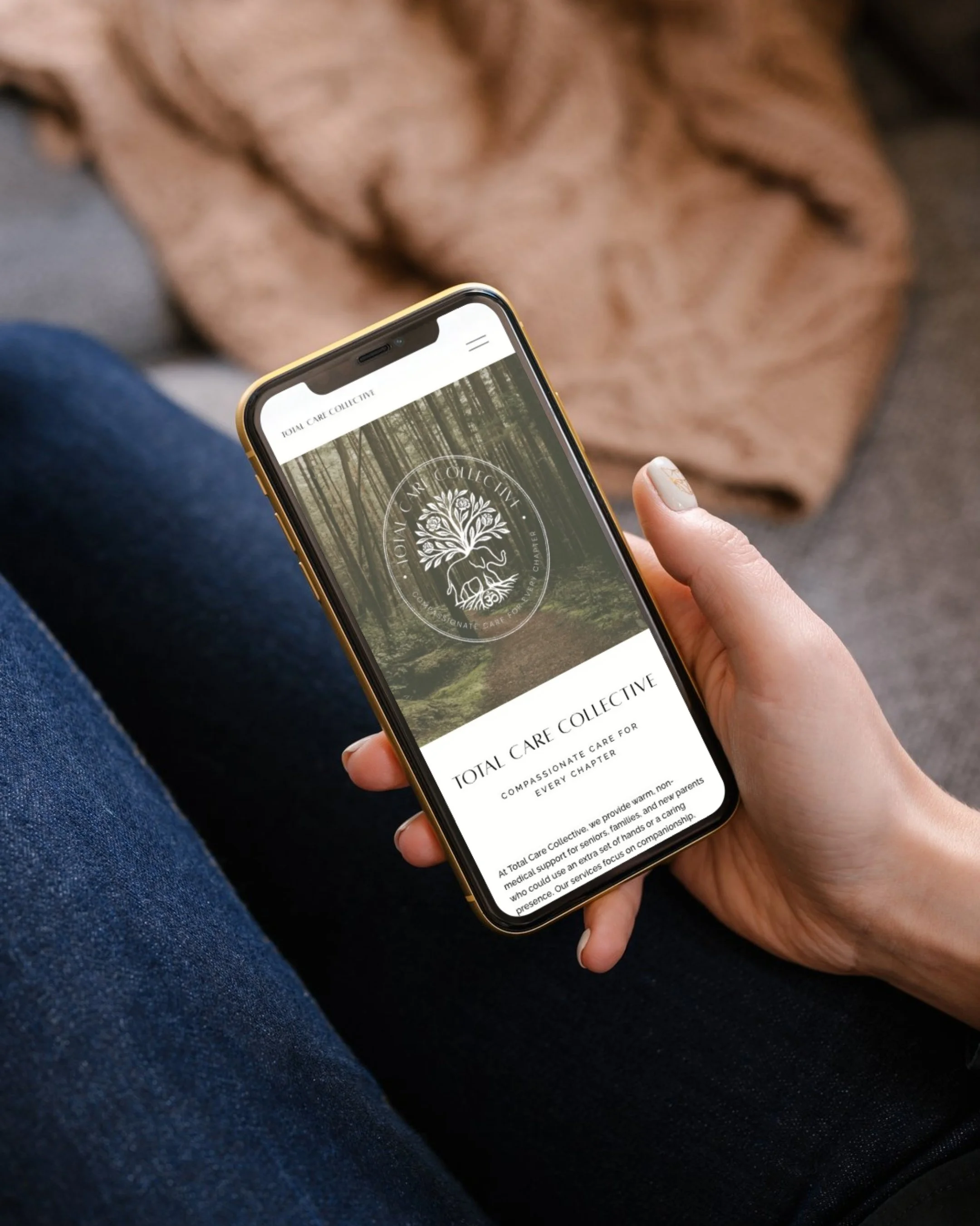 Person holding a smartphone displaying the Total Care Collective website, with a small dog sleeping on a blanket in the background.