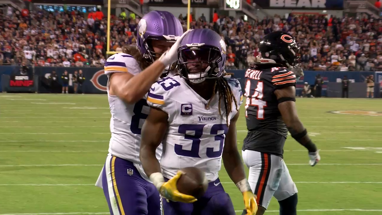 Two football players from the Minnesota Vikings celebrating after scoring a touchdown, with a Chicago Bears player in the background, on a football field during a game.