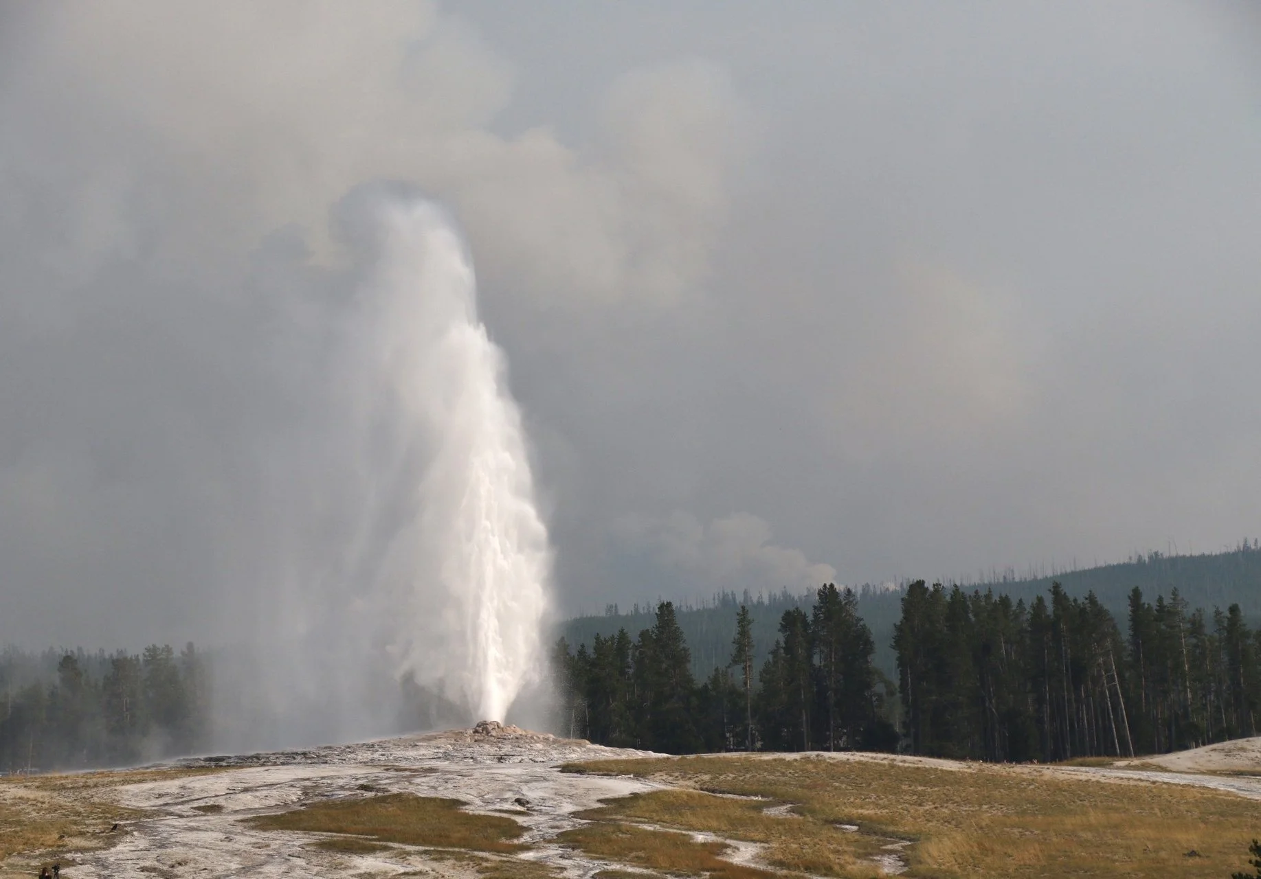 Smoke from the Lone Star Fire rises in the distance as Old Faithful erupts in Yellowstone National Park on August 23, 2020.