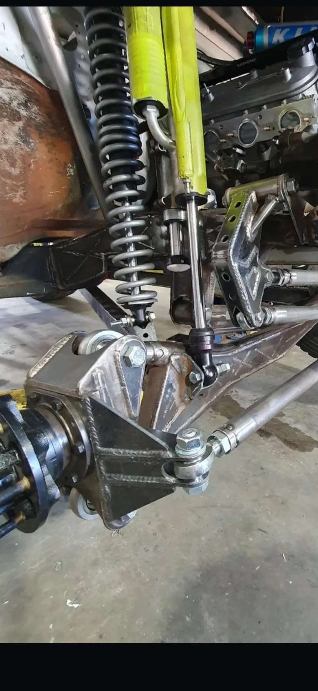 Close-up of a motorcycle front suspension and steering components, including a coil shock absorber, metal frame, and steering linkage.