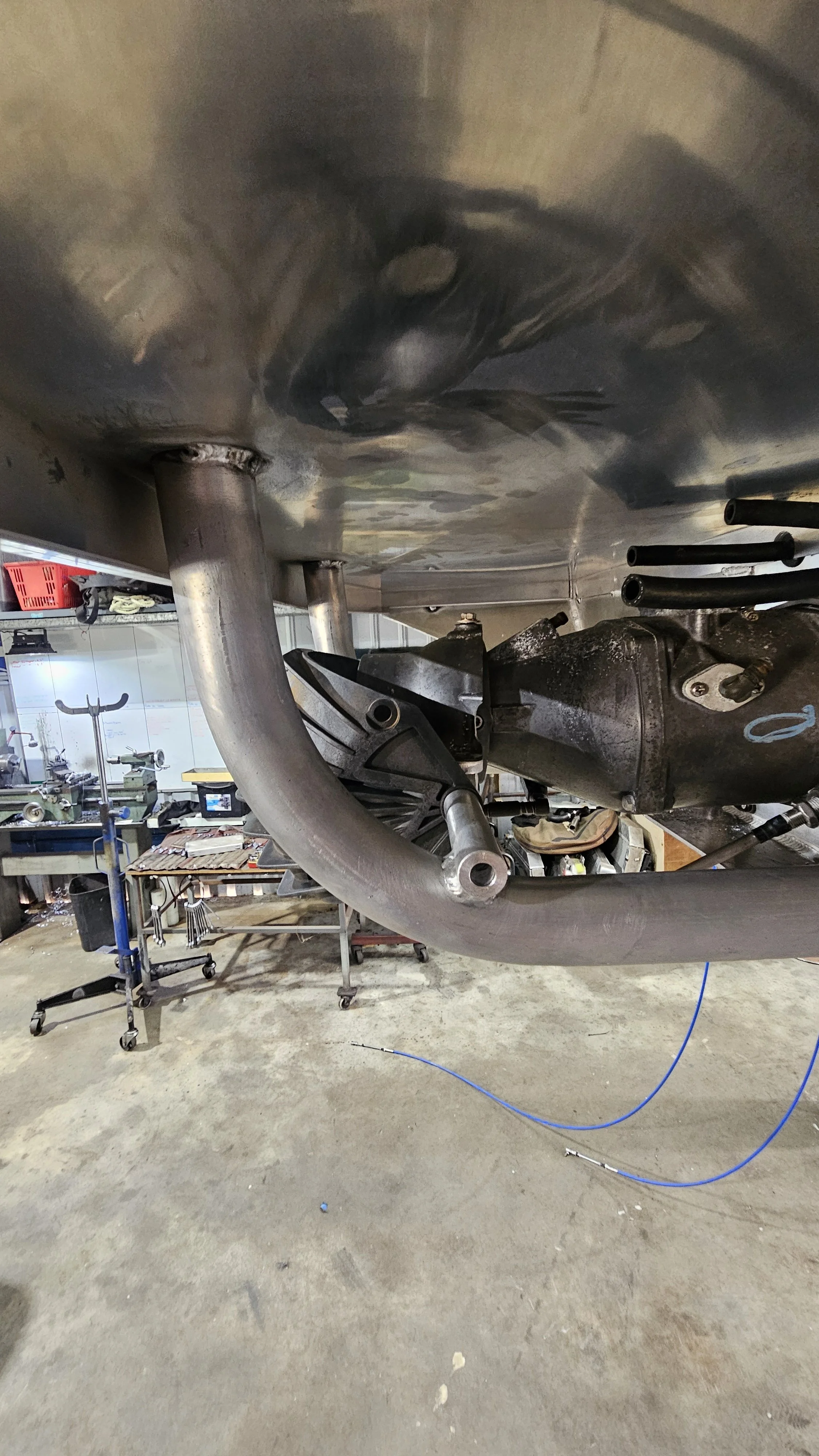  underside of a boat showing exhaust pipe and mechanical parts in a workshop.