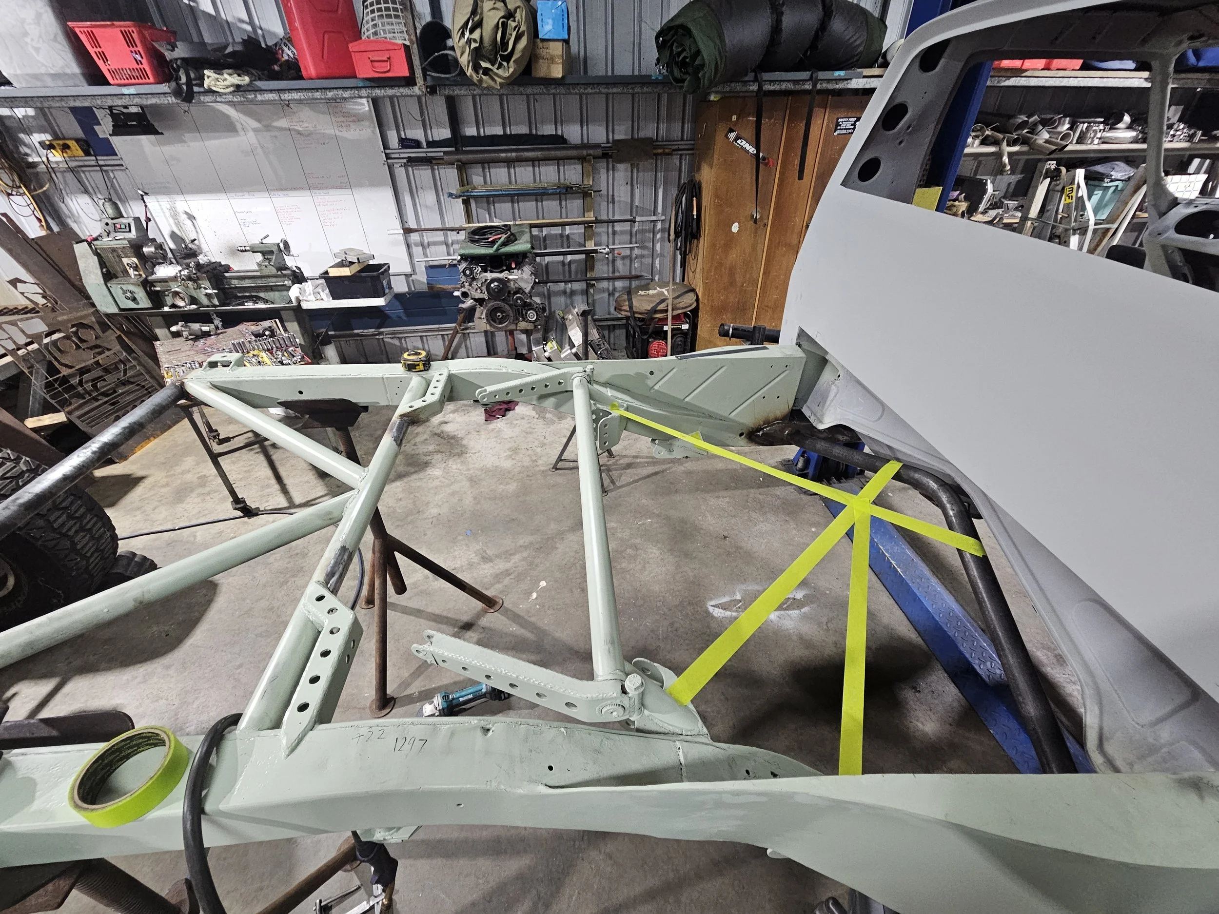 A car frame under construction in a workshop, with various tools and equipment around.