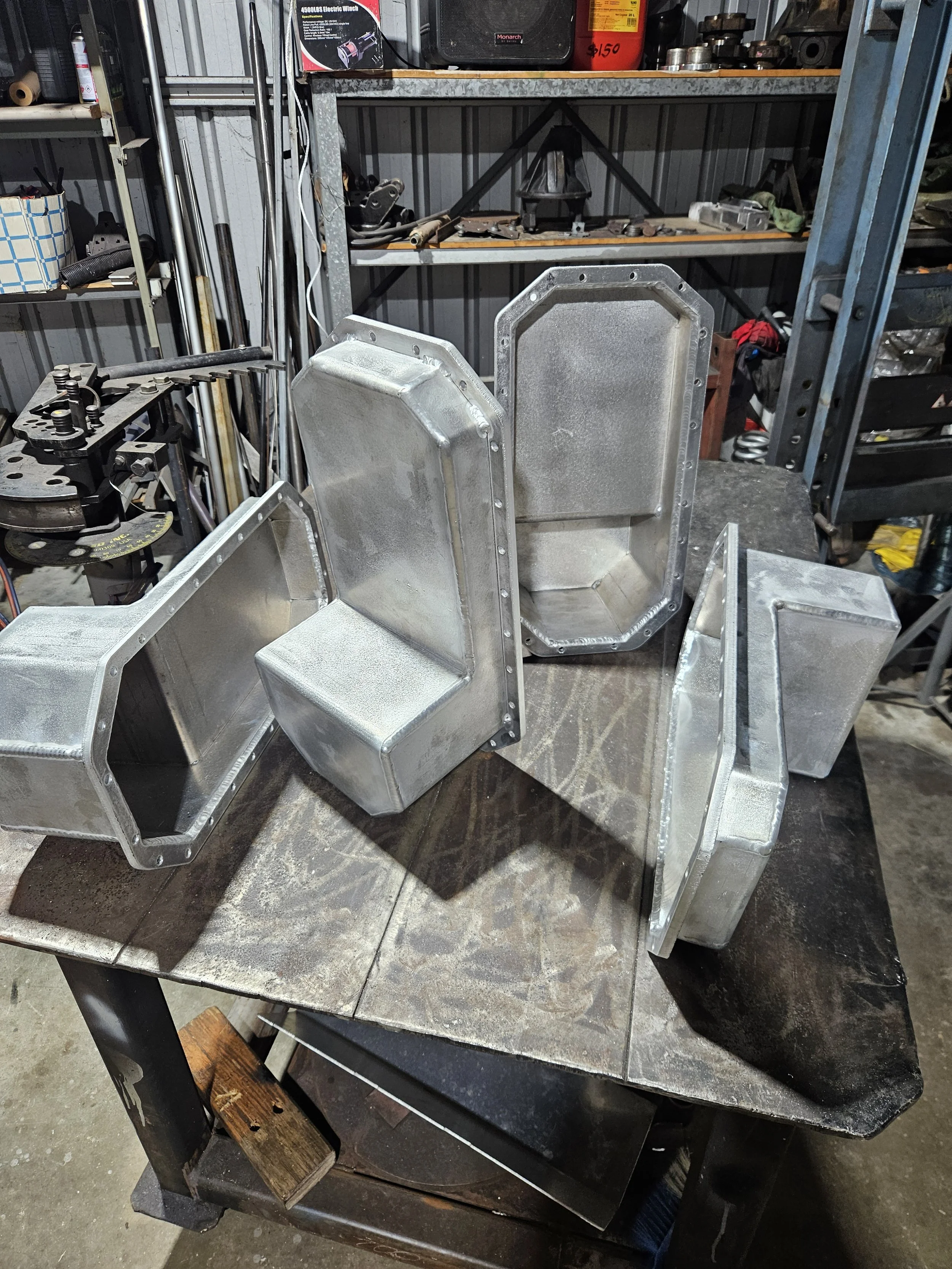 Three aluminum metal boxes with riveted edges on a workbench in a workshop.