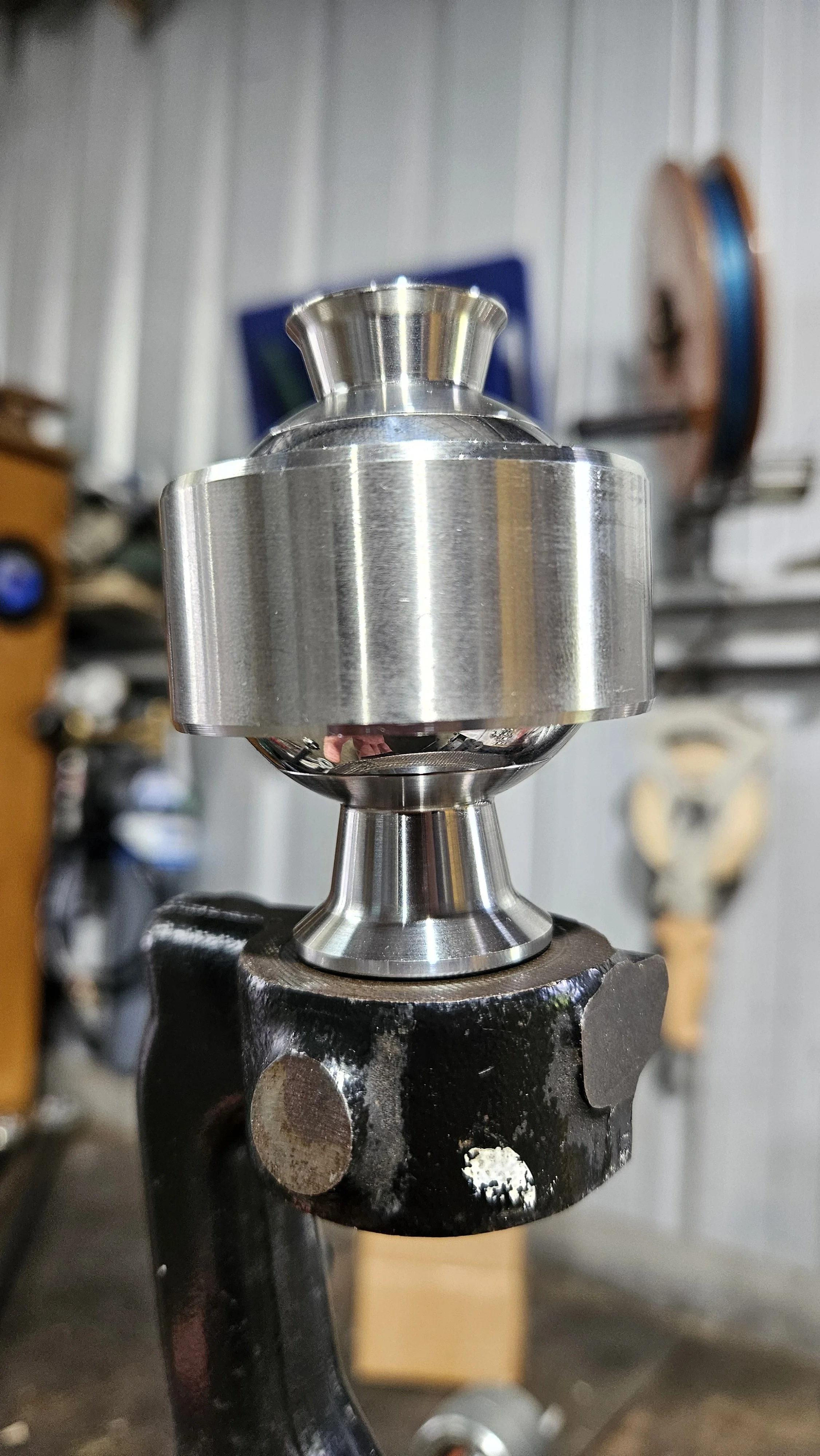 A shiny, metallic, spherical object mounted on a black workbench with a worn surface, in a workshop setting.