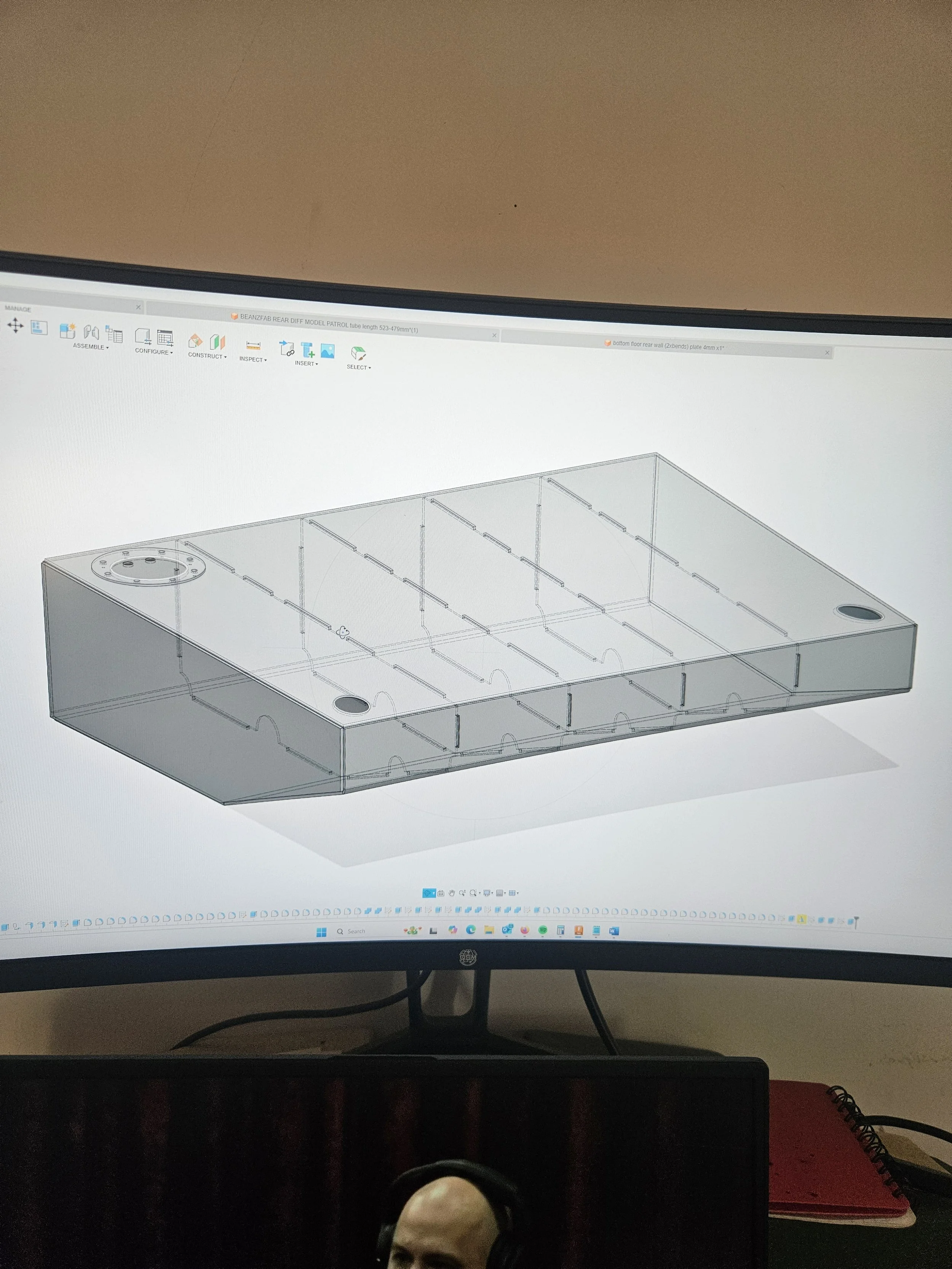 A computer screen displaying a 3D CAD design of a rectangular object with multiple compartments and two circular openings on the top surface.
