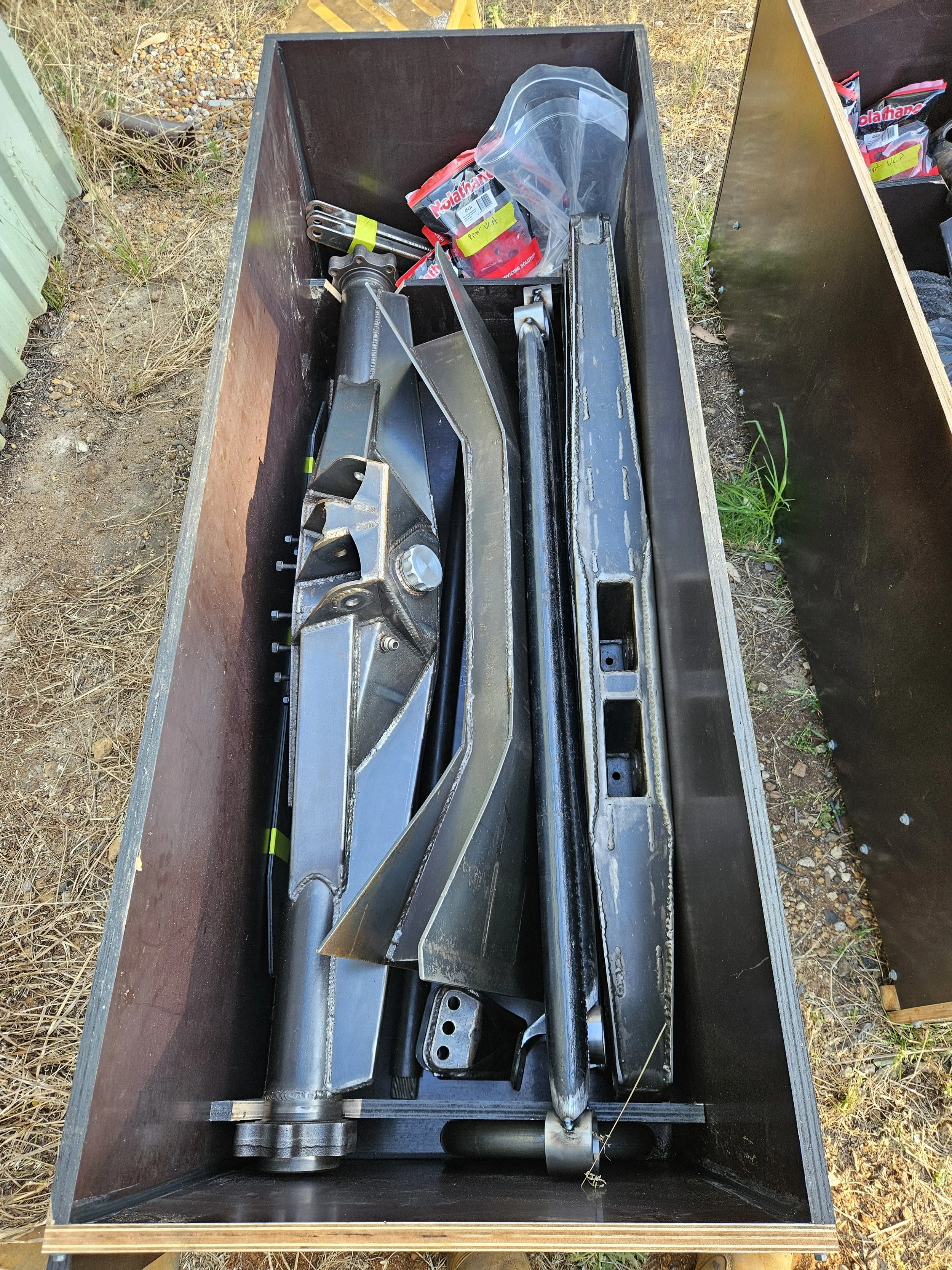Metal construction tools and parts in a wooden storage bin outdoors.