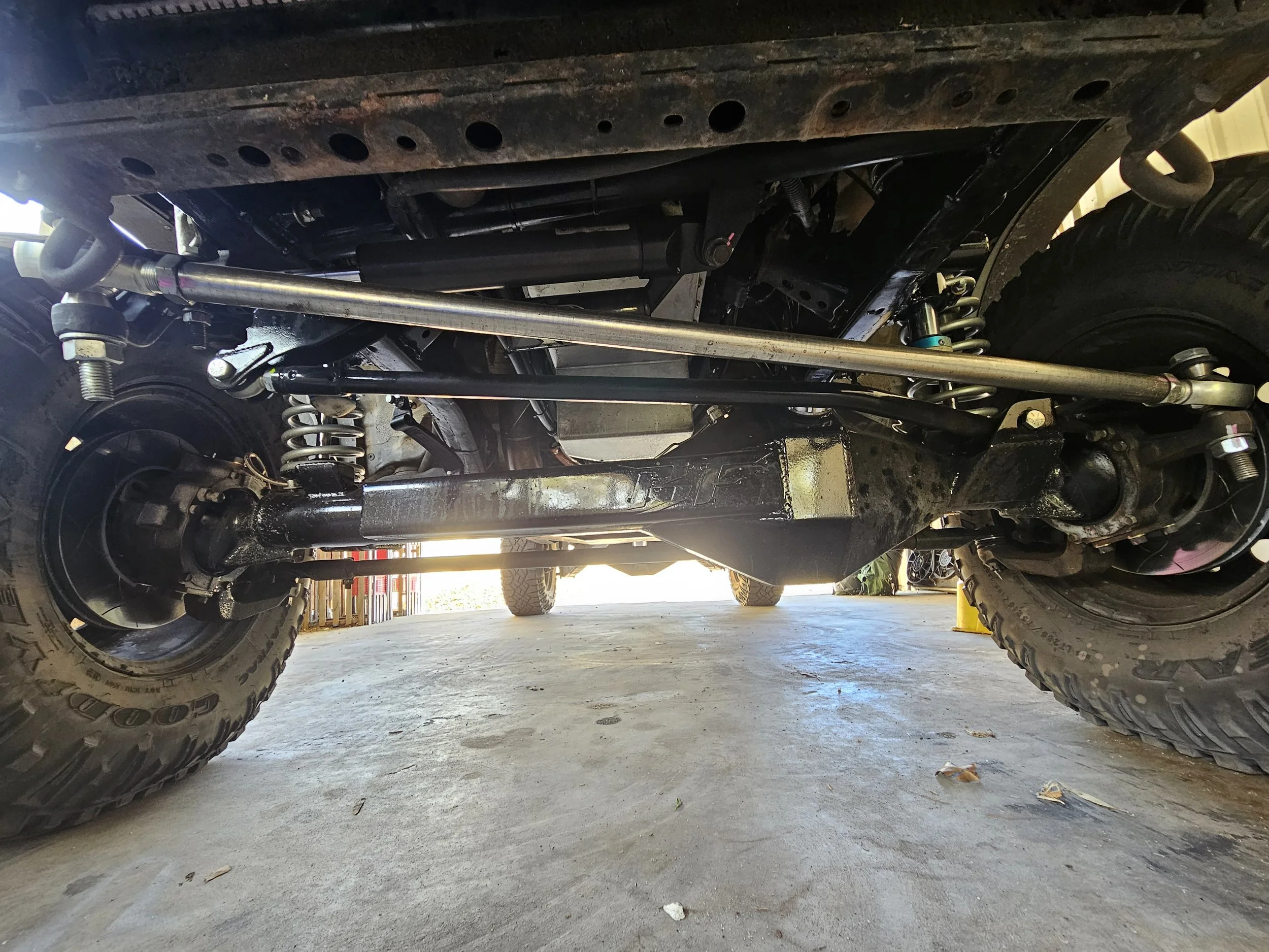 Underneath view of a vehicle showing suspension components, tires, and a metal bar.