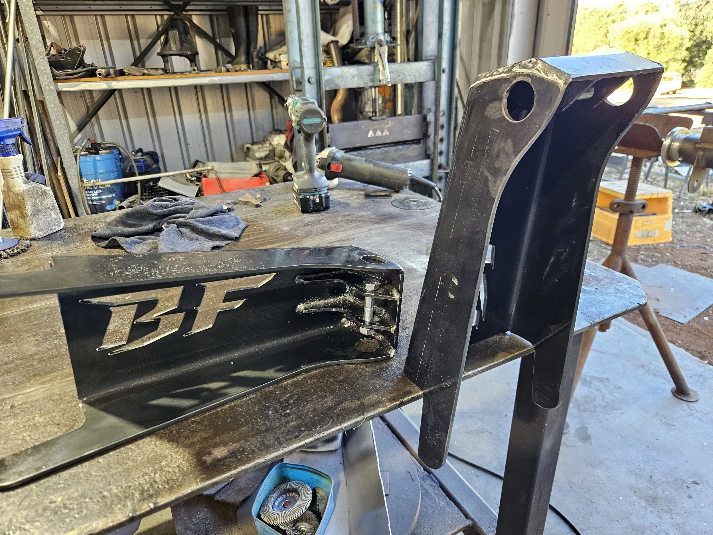 Metal bracket with 'BF' logo on a workbench in a workshop, surrounded by tools and equipment.