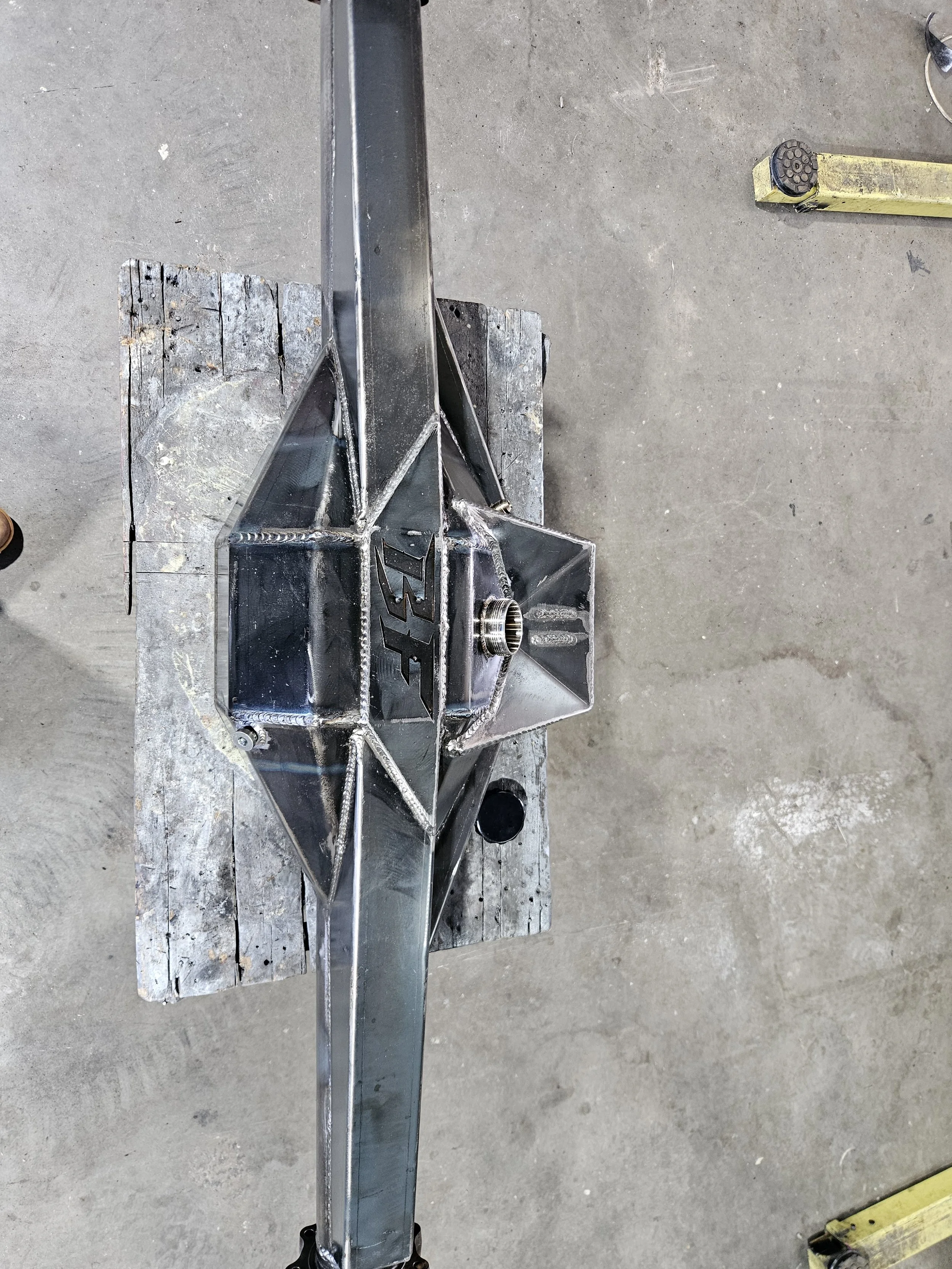 A metal race car chassis being assembled on a wooden workbench in a workshop.