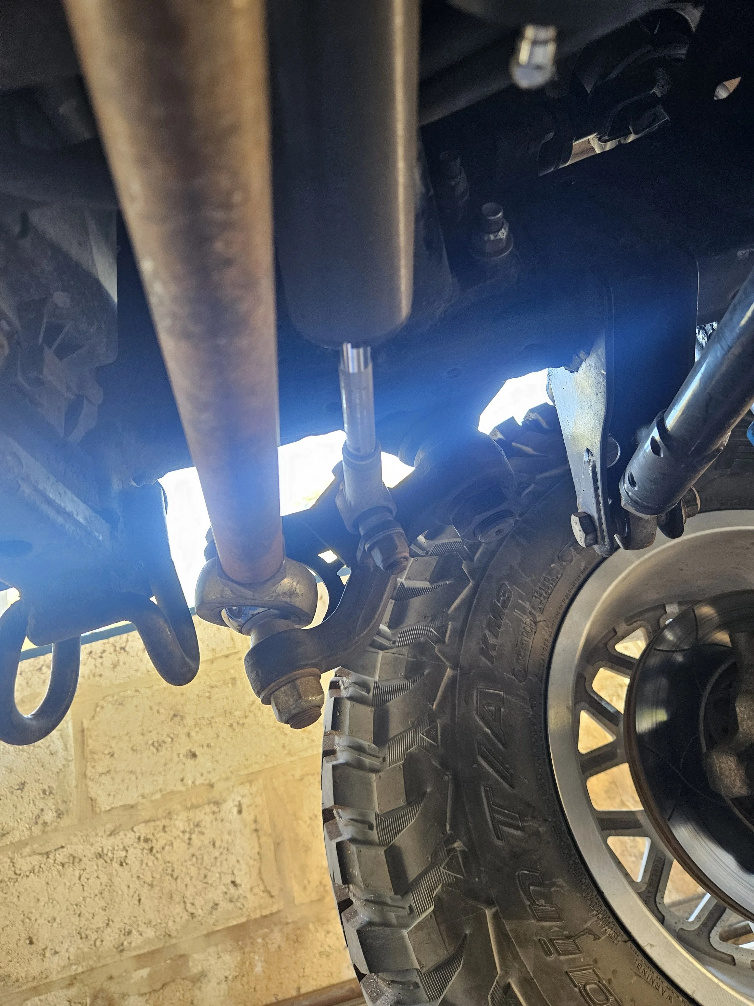 Close-up view of the underside of a vehicle showing parts of the suspension and a large off-road tire.