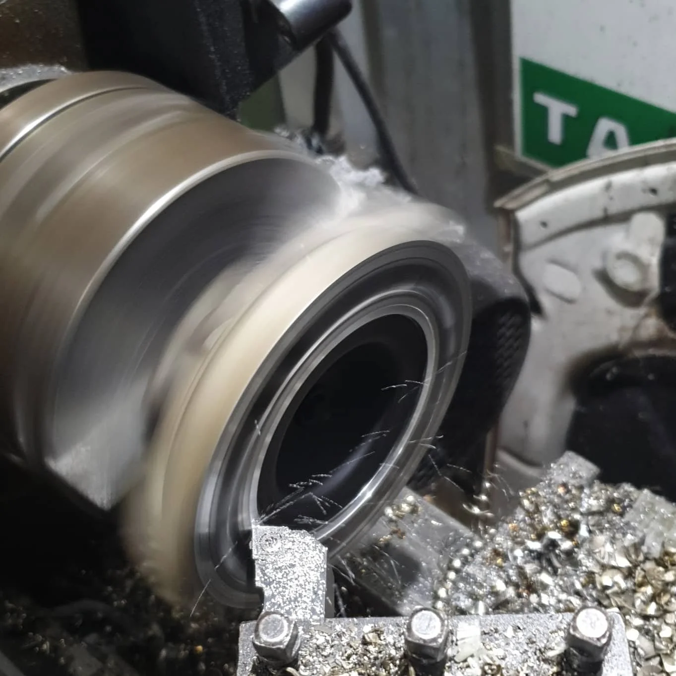 A metal grinding or machining process on a cylindrical metal part, with metal shavings and sparks around.
