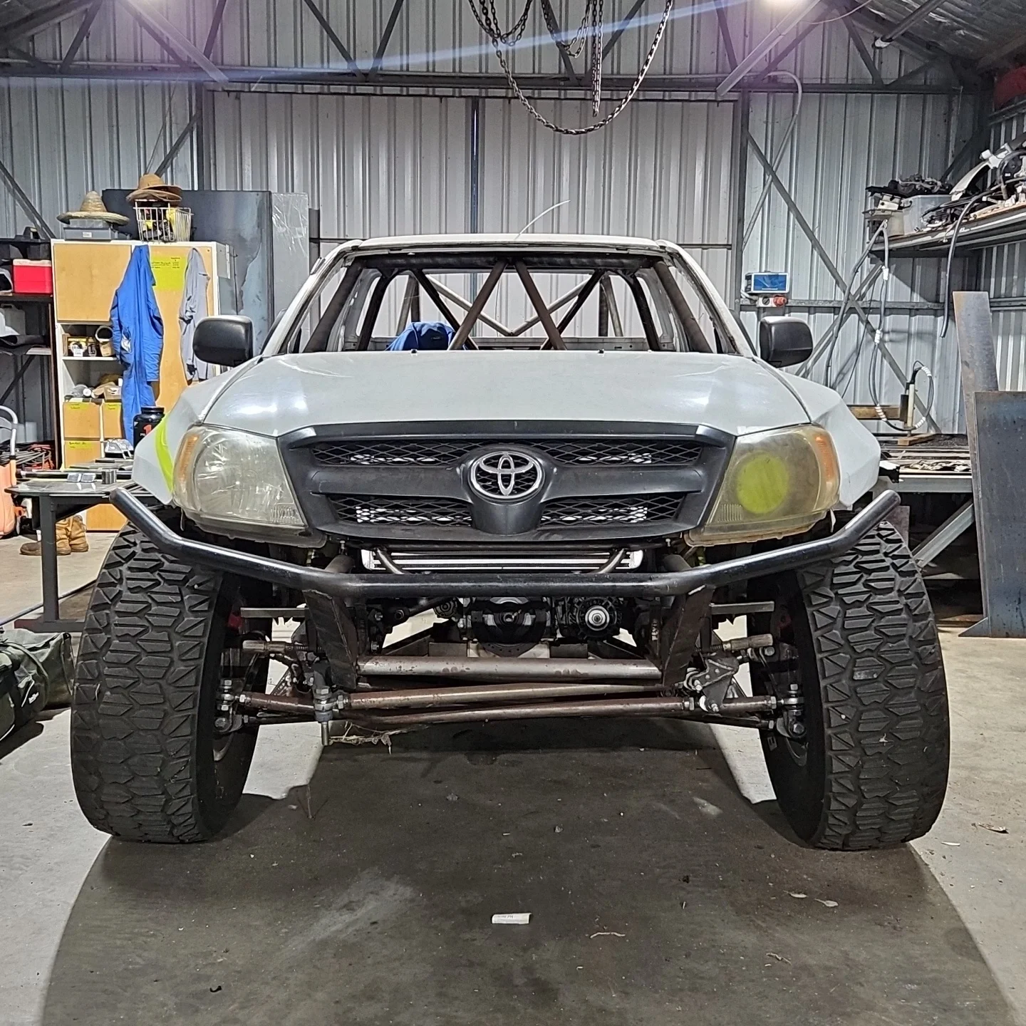 Front view of a race car inside a workshop, with large tires, a roll cage, and a Toyota badge on the front grille.