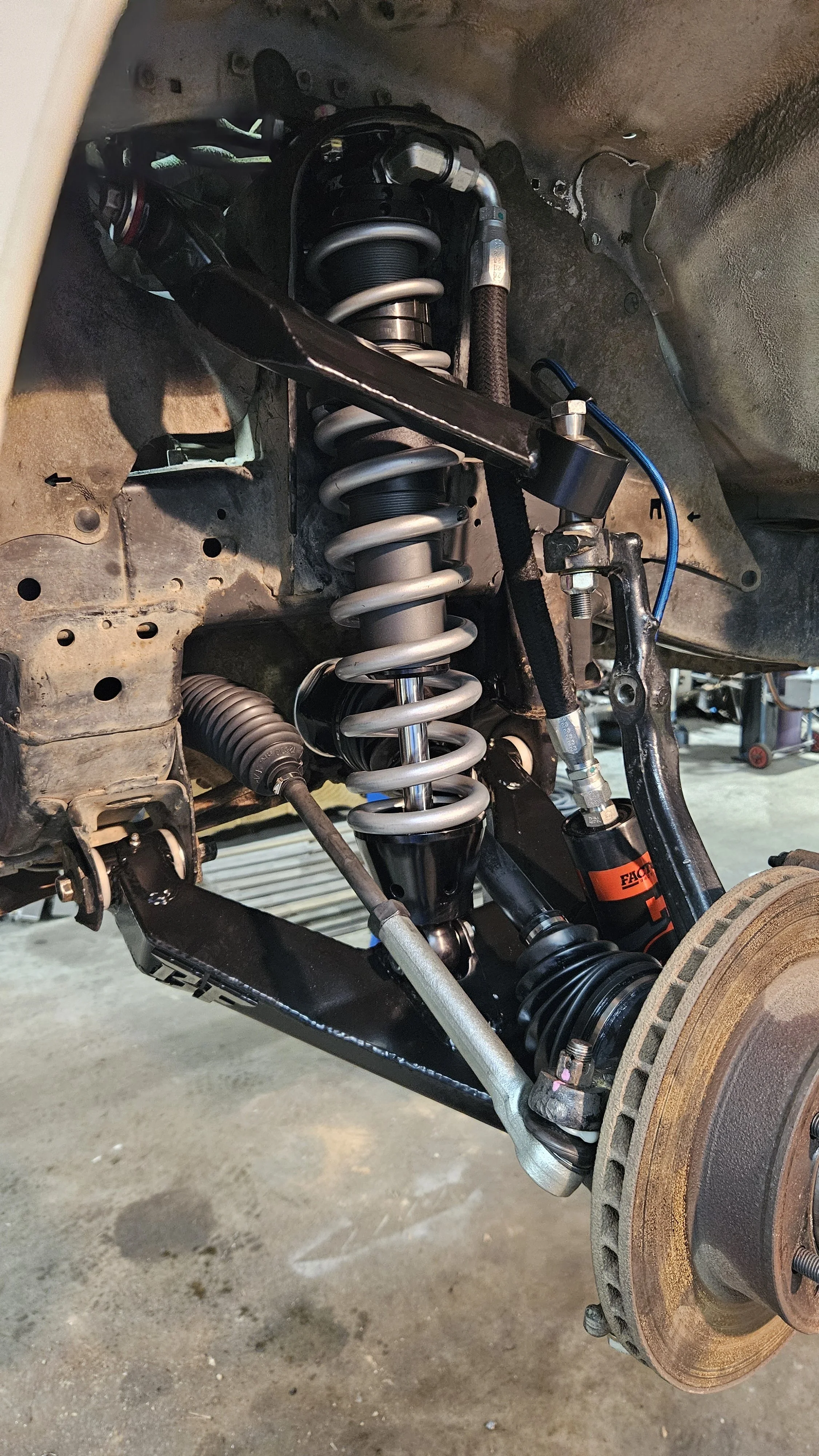 Close-up of a vehicle's suspension system, including shock absorbers, coil spring, and brake rotor.