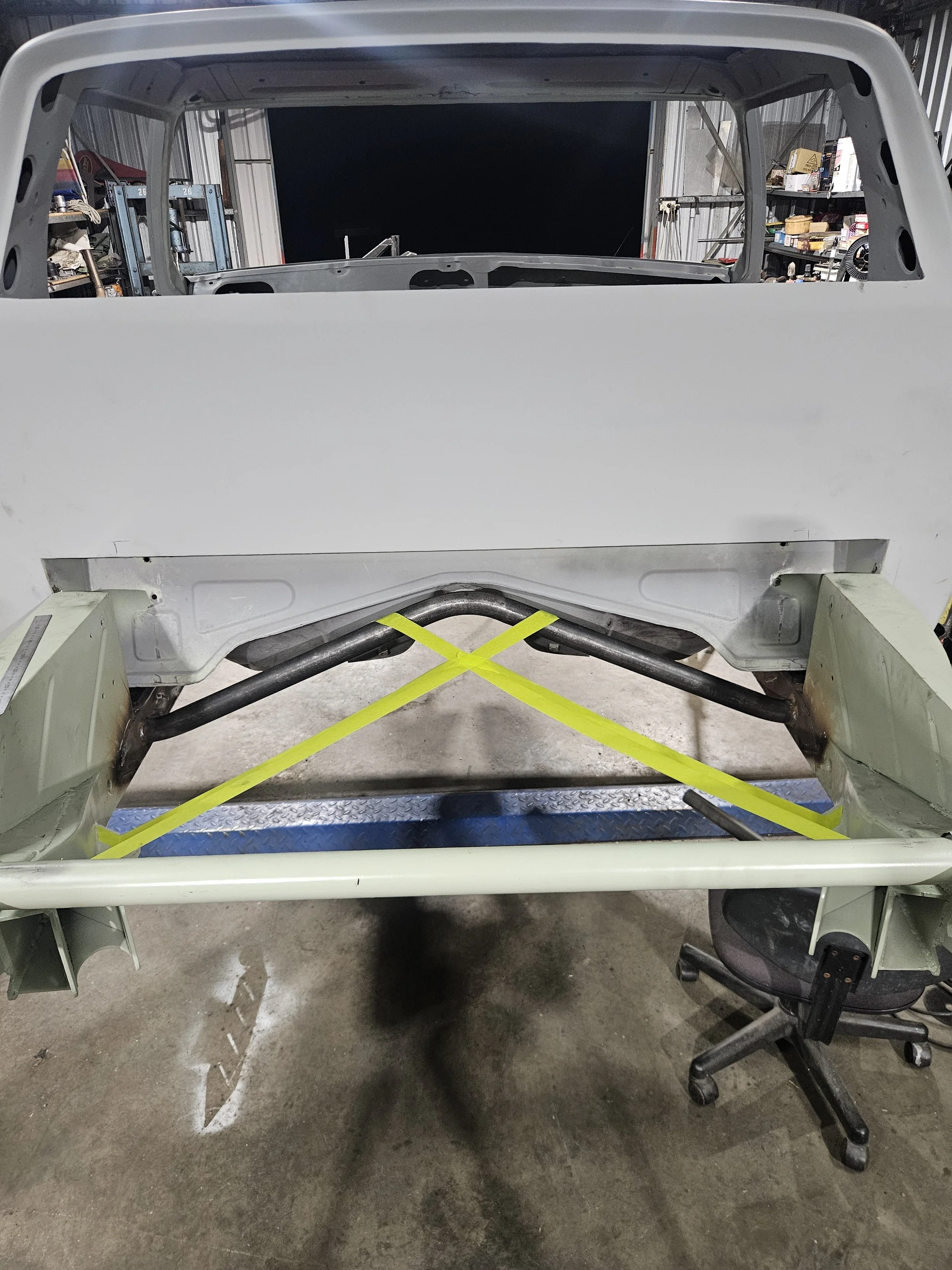 Partially assembled car body frame on a stand with yellow straps in a workshop.