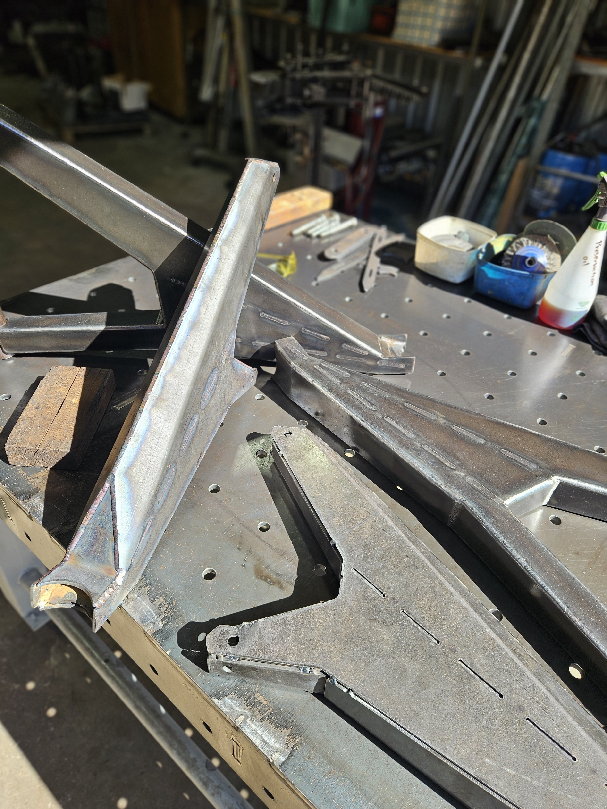 Metal parts and tools on a metal workbench in a workshop, with a partially assembled metal structure.