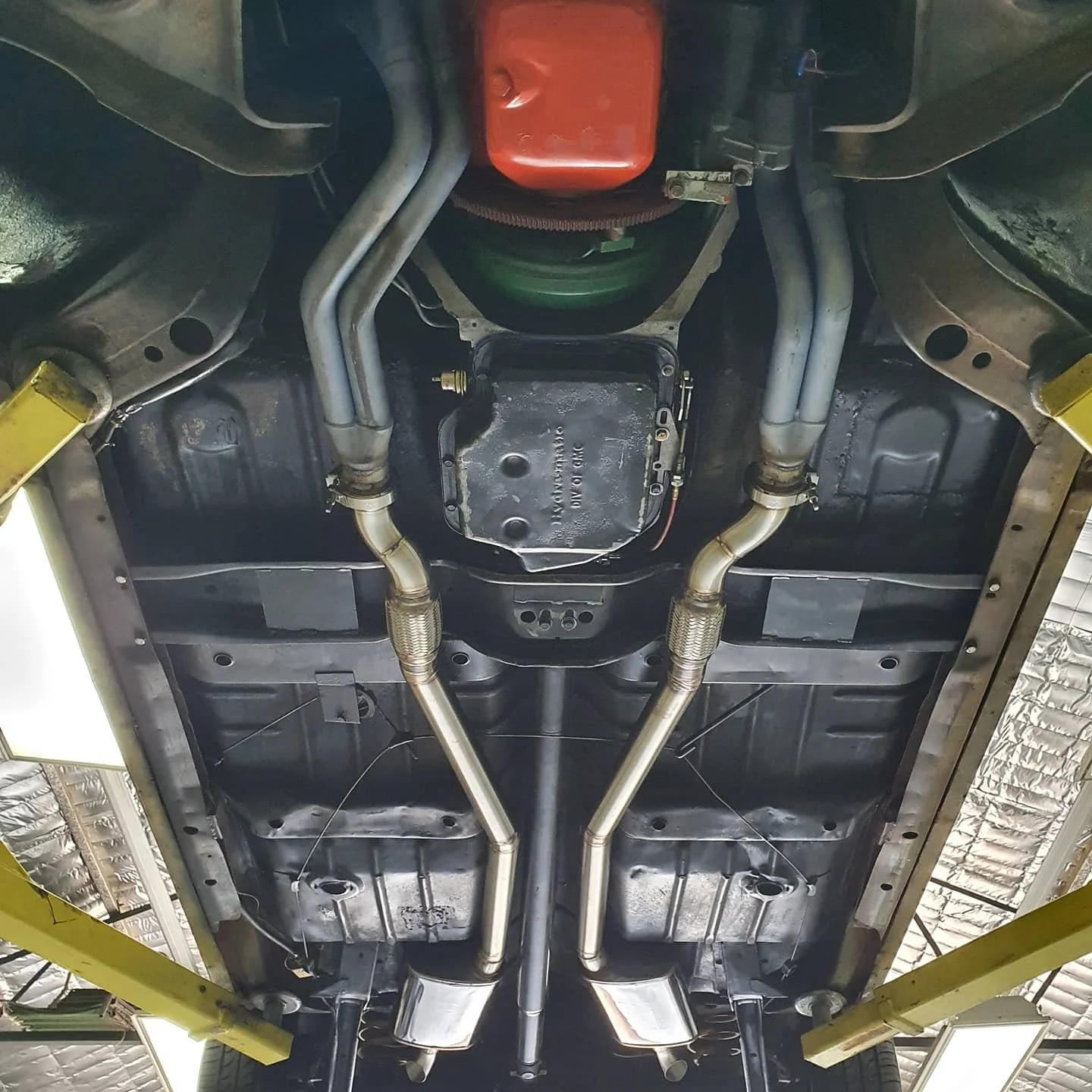 Underside of a car showing exhaust system, oil pan, and suspension components in a garage or workshop.