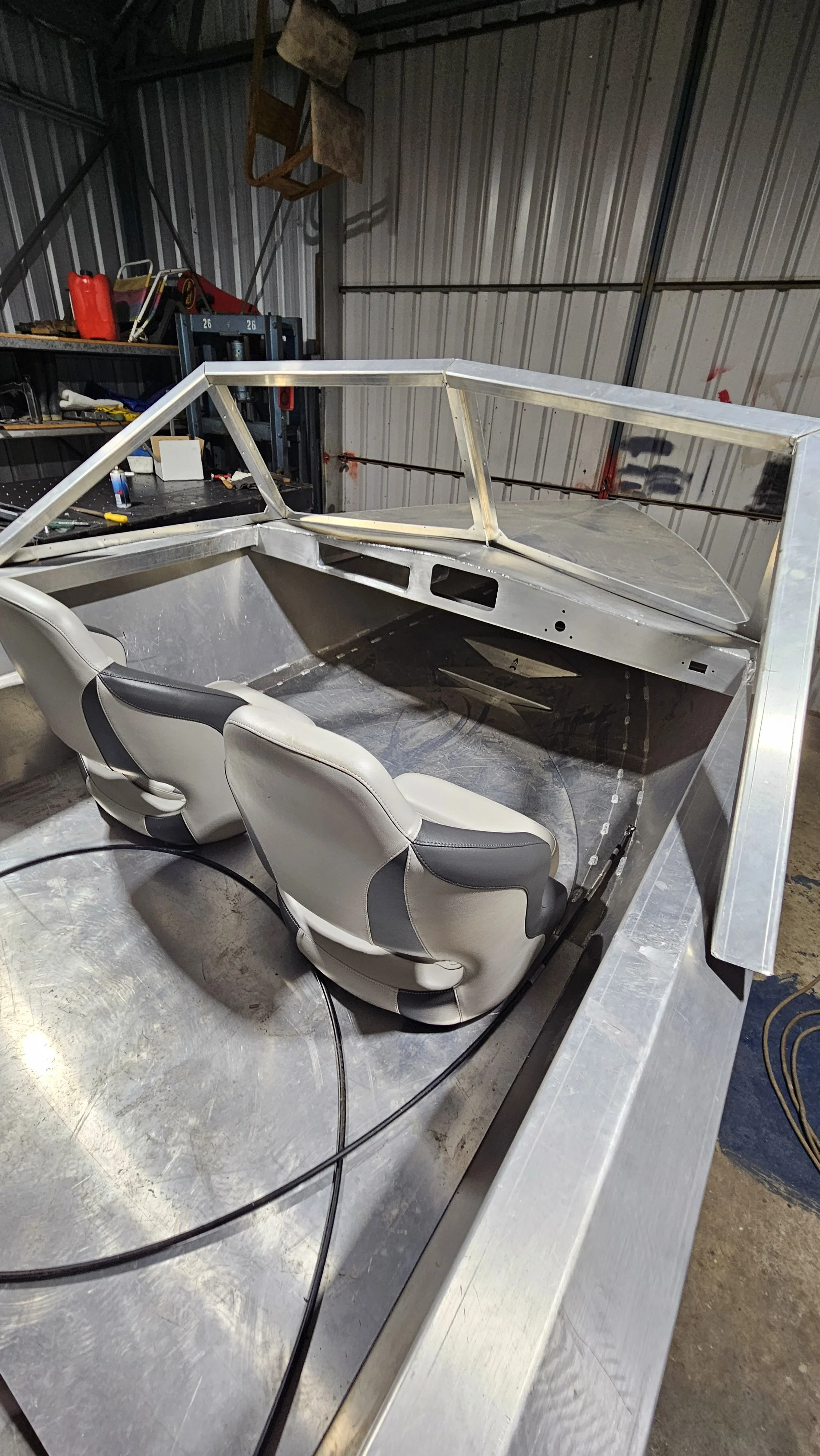 Partially assembled small vehicle or cardboard frame with two white and black seats inside a workshop or garage.