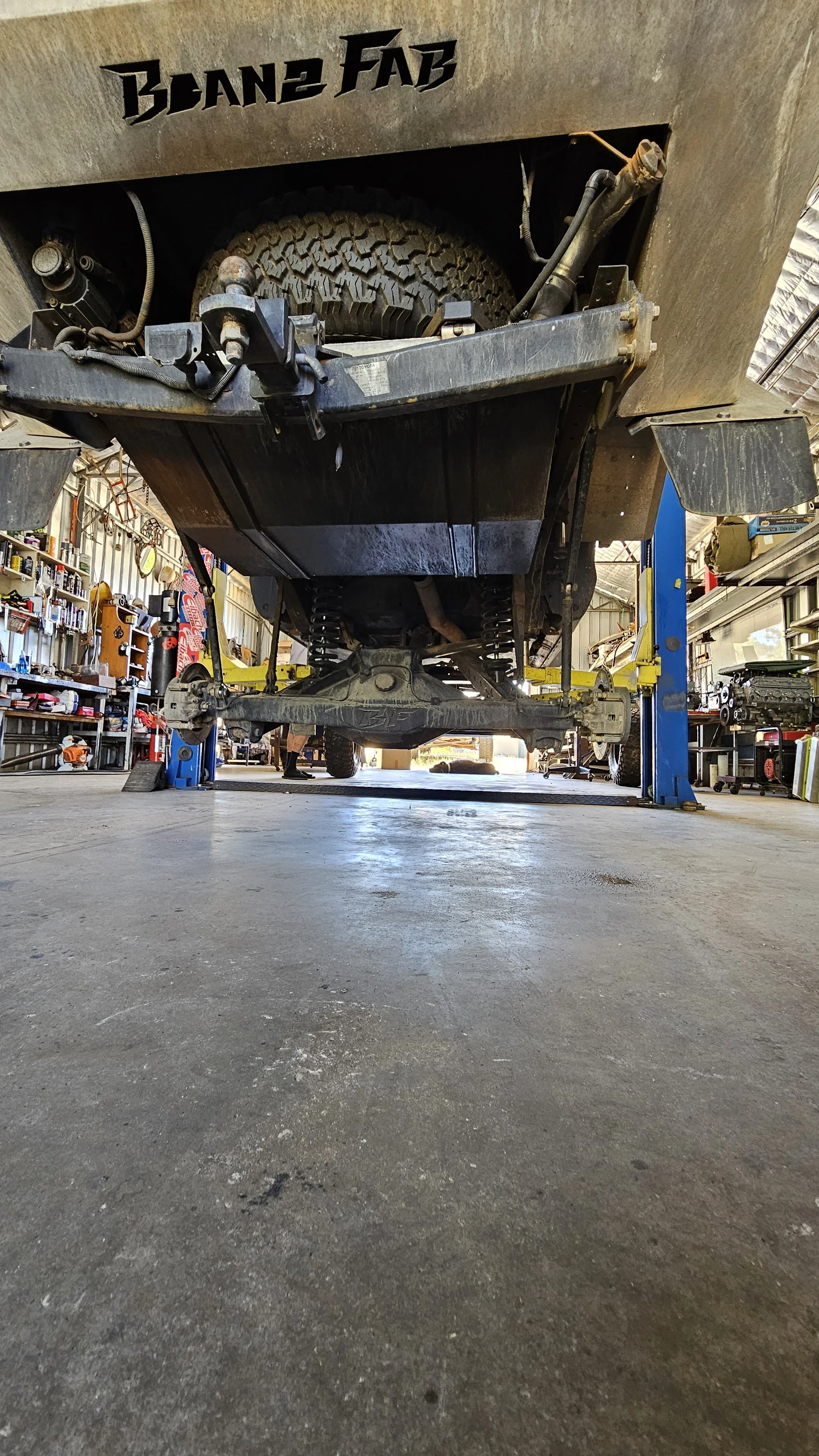 Front view of a lifted off-road vehicle in a garage, showing its suspension, tires, and undercarriage part.