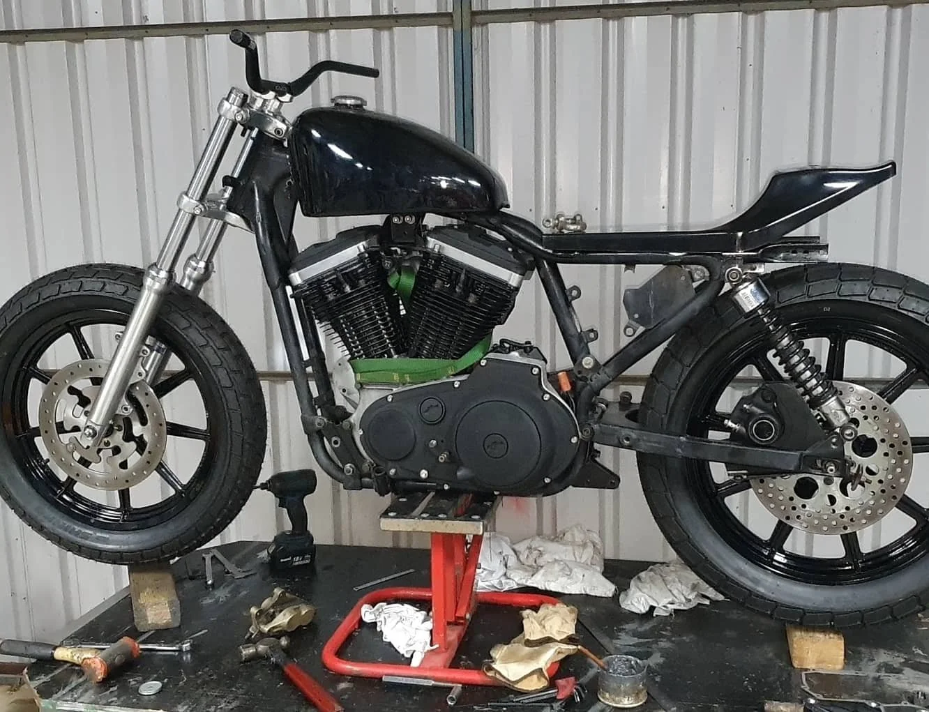 A black motorcycle on a red stand in a workshop, with tools and parts scattered around, partially assembled with the bodywork removed.