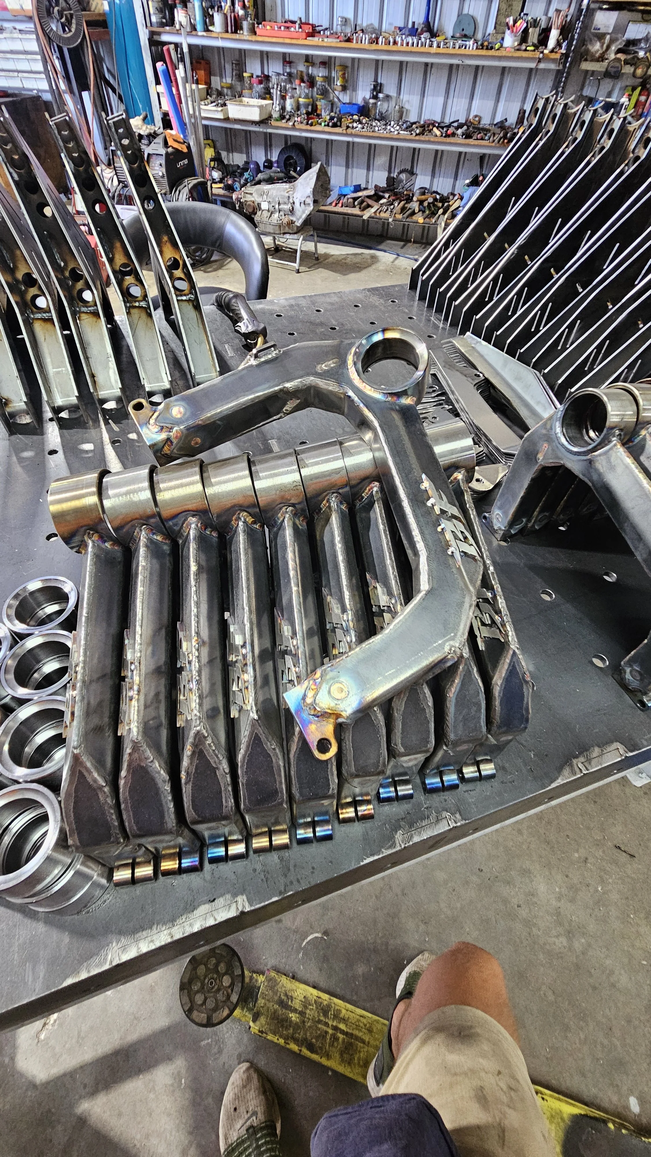 Metal engine parts arranged on a workbench in a workshop, with shelves of tools and components in the background.
