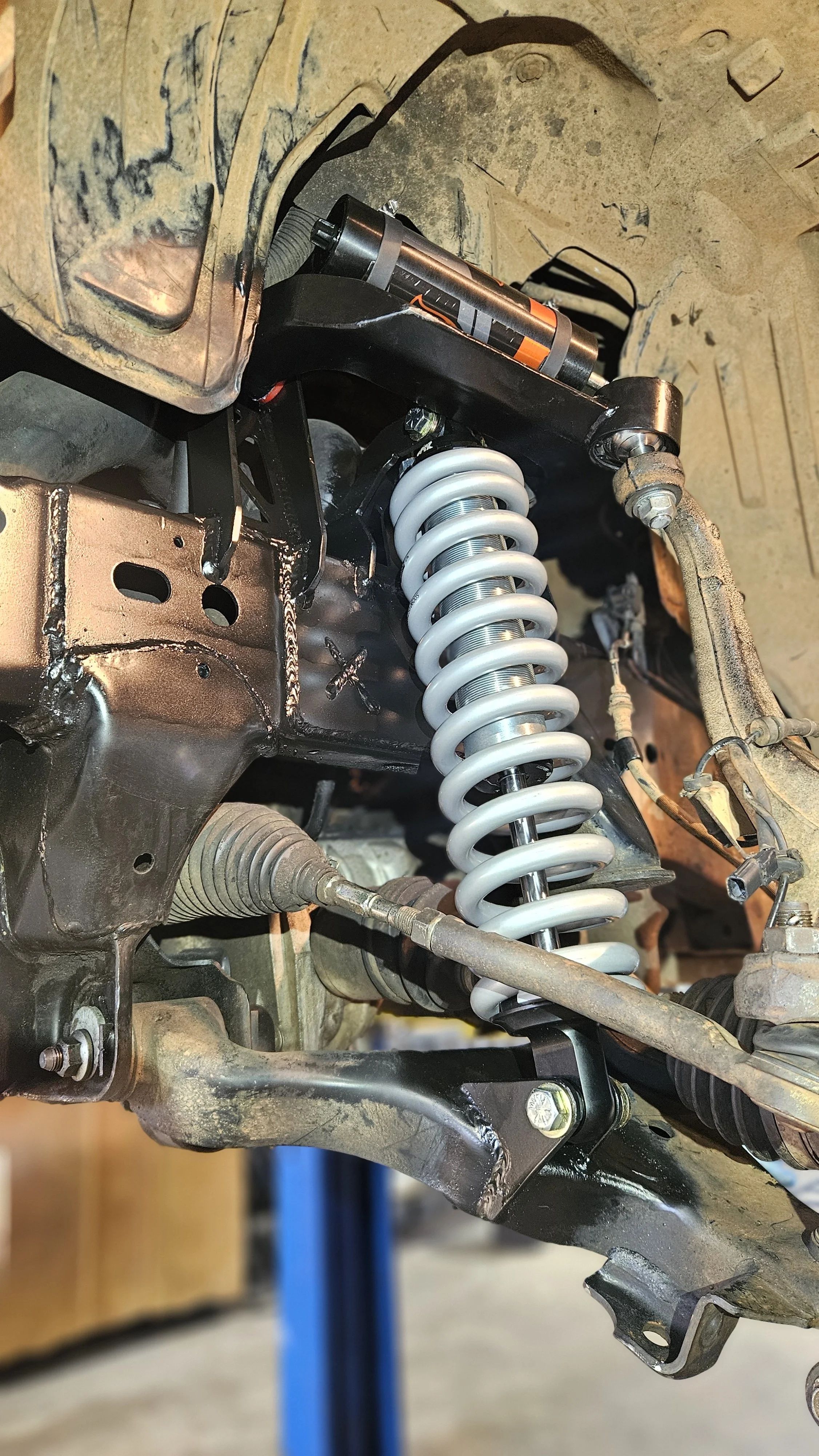 Close-up of a vehicle's suspension system, showing a coil spring, shock absorber, and metal components resting on a workbench.