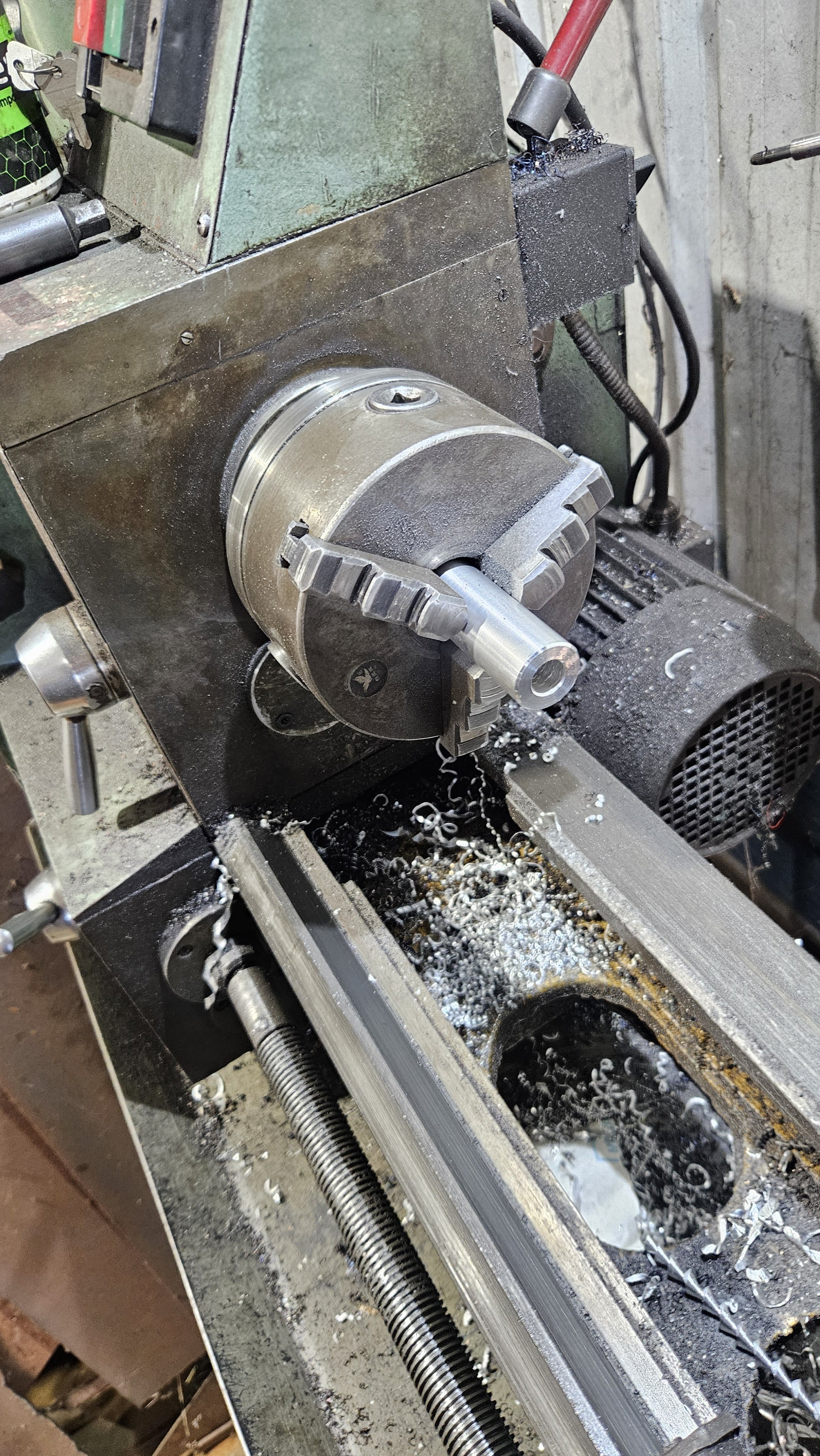 A metal lathe machine in operation, shaping a metal workpiece with shavings and coolant spray visible.