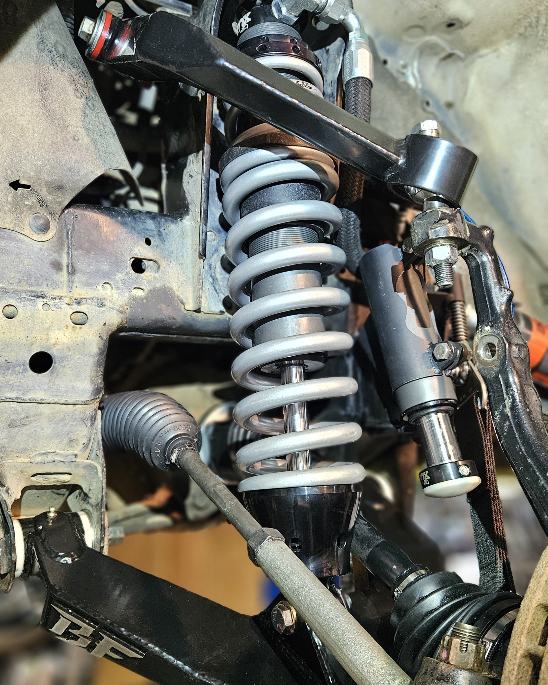 Close-up of a vehicle's suspension system, including a coil spring, shock absorber, and steering linkage.